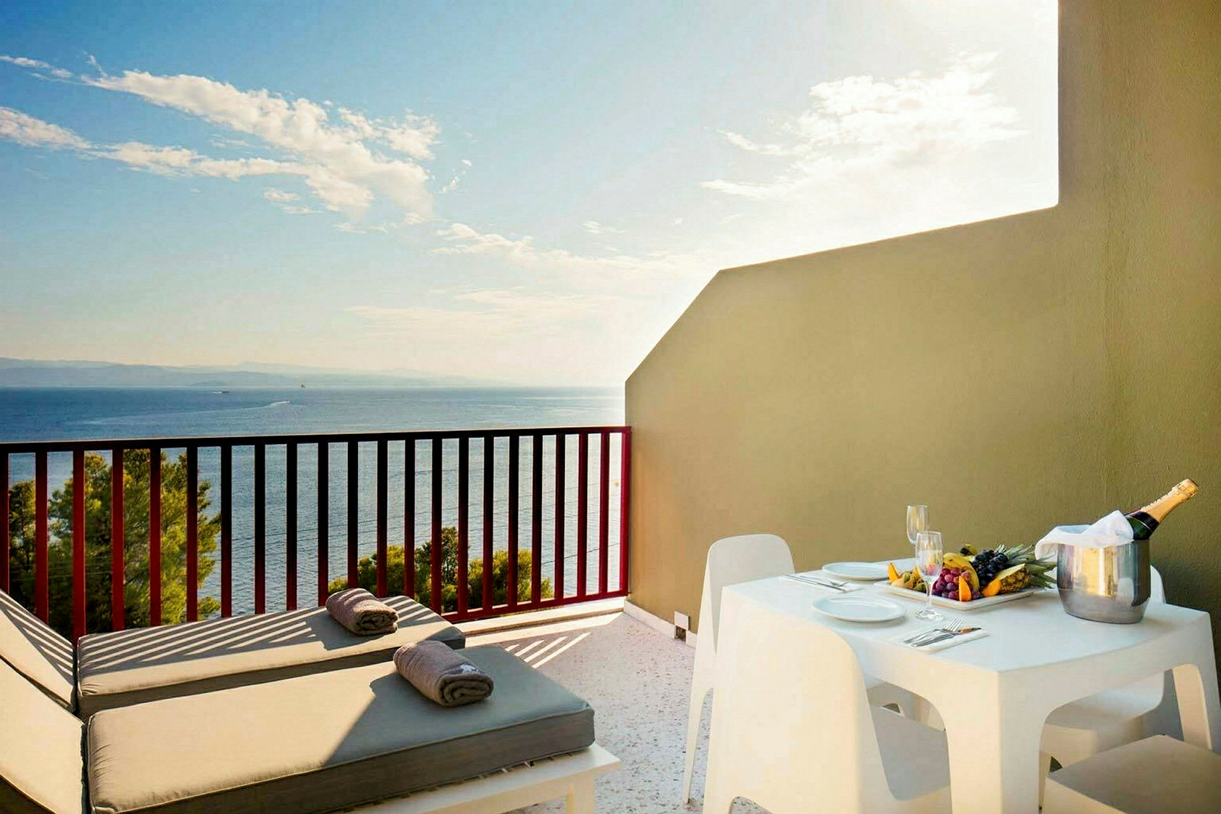 En terrasse med solsenger, bord og stoler, samt utsikt mot havet. (AI-generert tekst)