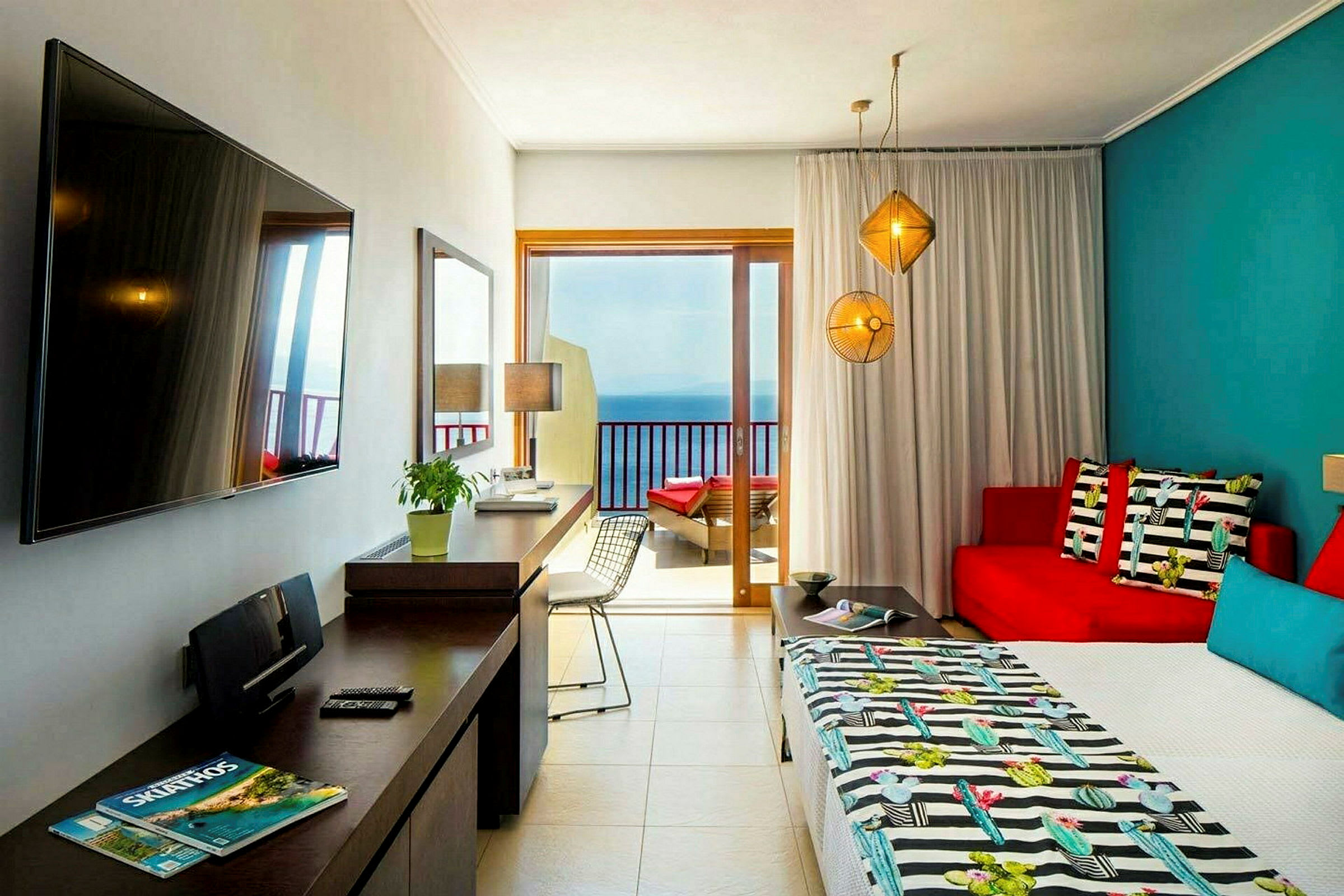 Et hotellrom med fargerikt interiør, en seng, sofa, bord og en balkongdør som vender mot havet. (AI-generert tekst)