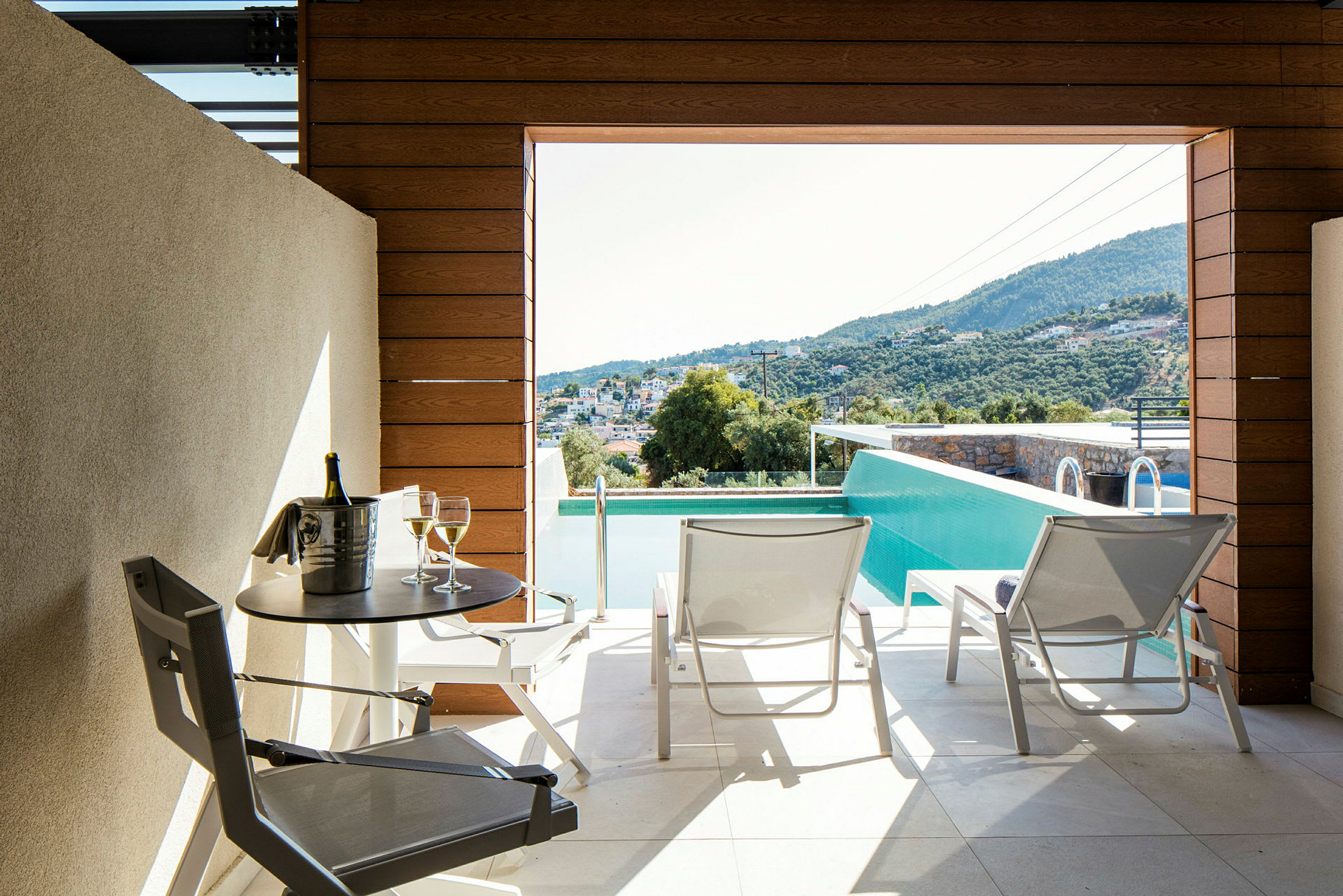 Terrasse med utsikt over bassenget og landskapet, med to solsenger og et bord med en flaske og to glass. (AI-generert tekst)