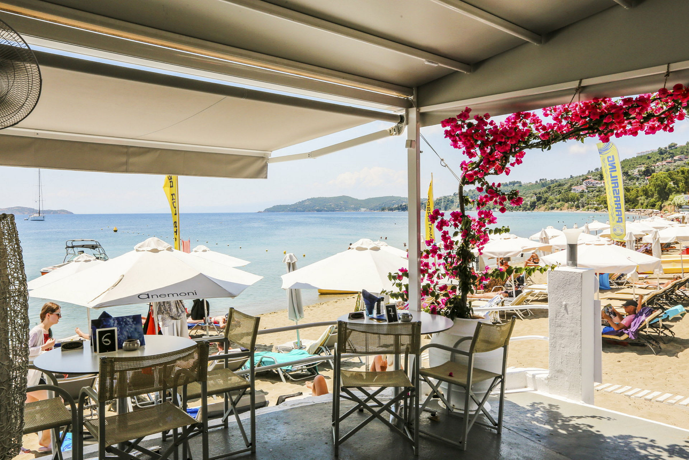 Utsikt fra en restaurant mot en strand med parasoller og solsenger ved havet. (AI-generert tekst)