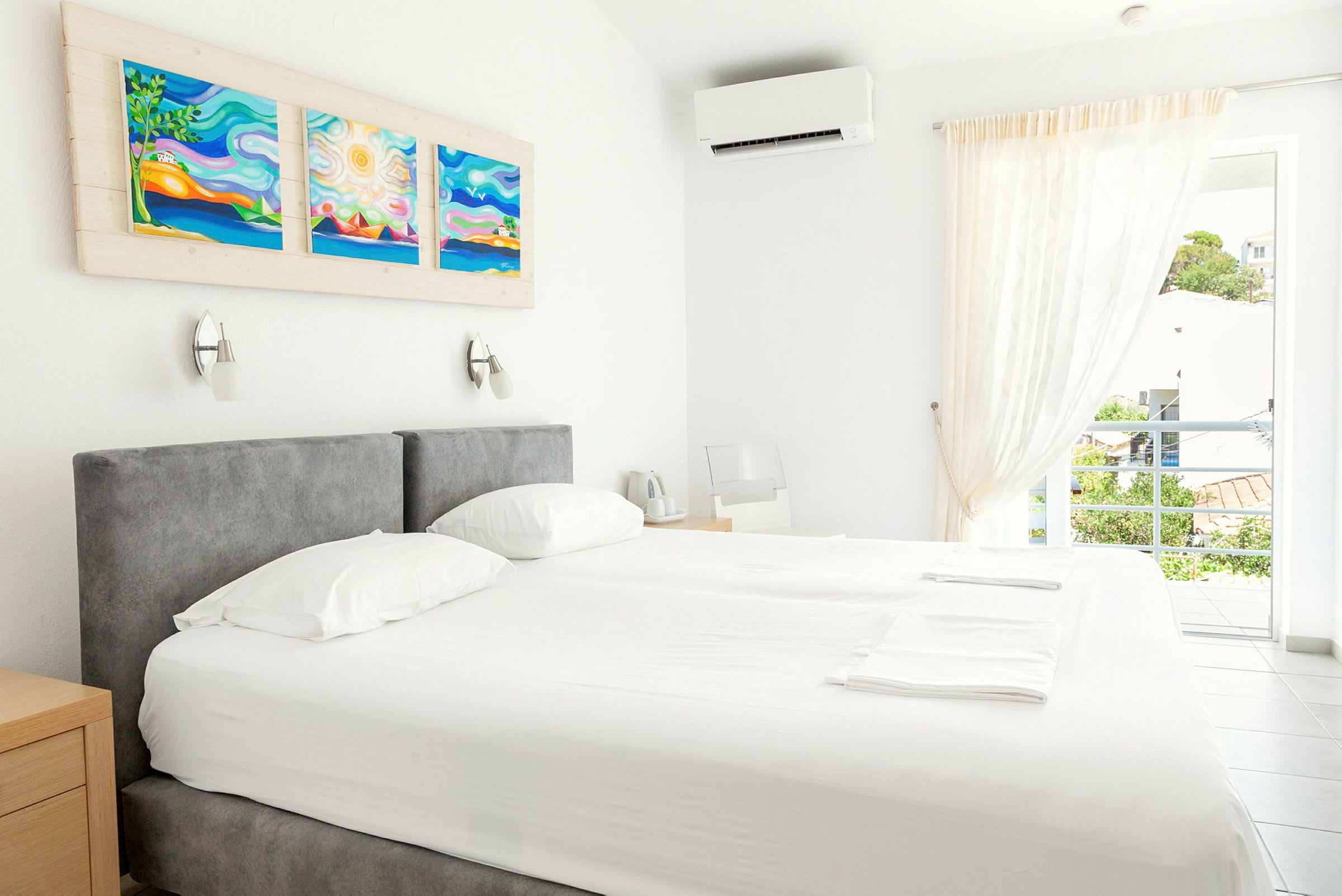 Et lyst hotellrom med dobbeltseng, kunstverk på veggen og et åpent vindu med utsikt. (AI-generert tekst)