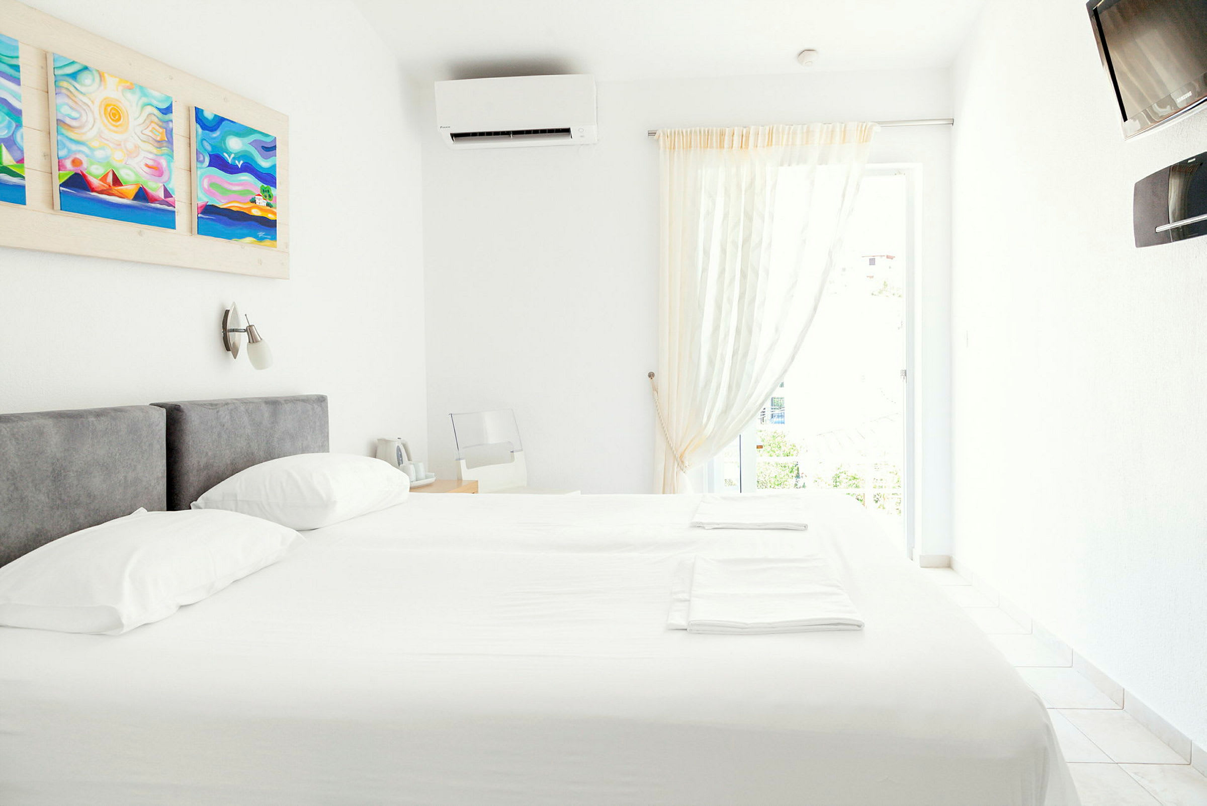 Et lyst og moderne innredet hotellrom med en dobbeltseng, veggkunst og klimaanlegg. (AI-generert tekst)