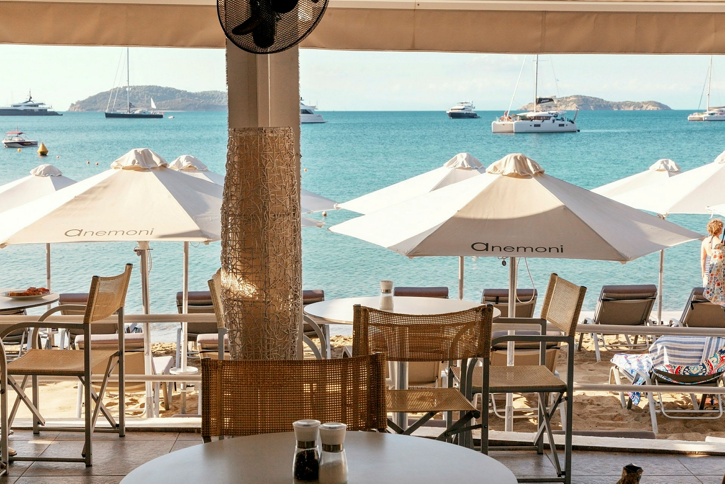 Utsikt fra en terrasse mot stranden med solsenger, parasoller og havet i bakgrunnen. (AI-generert tekst)