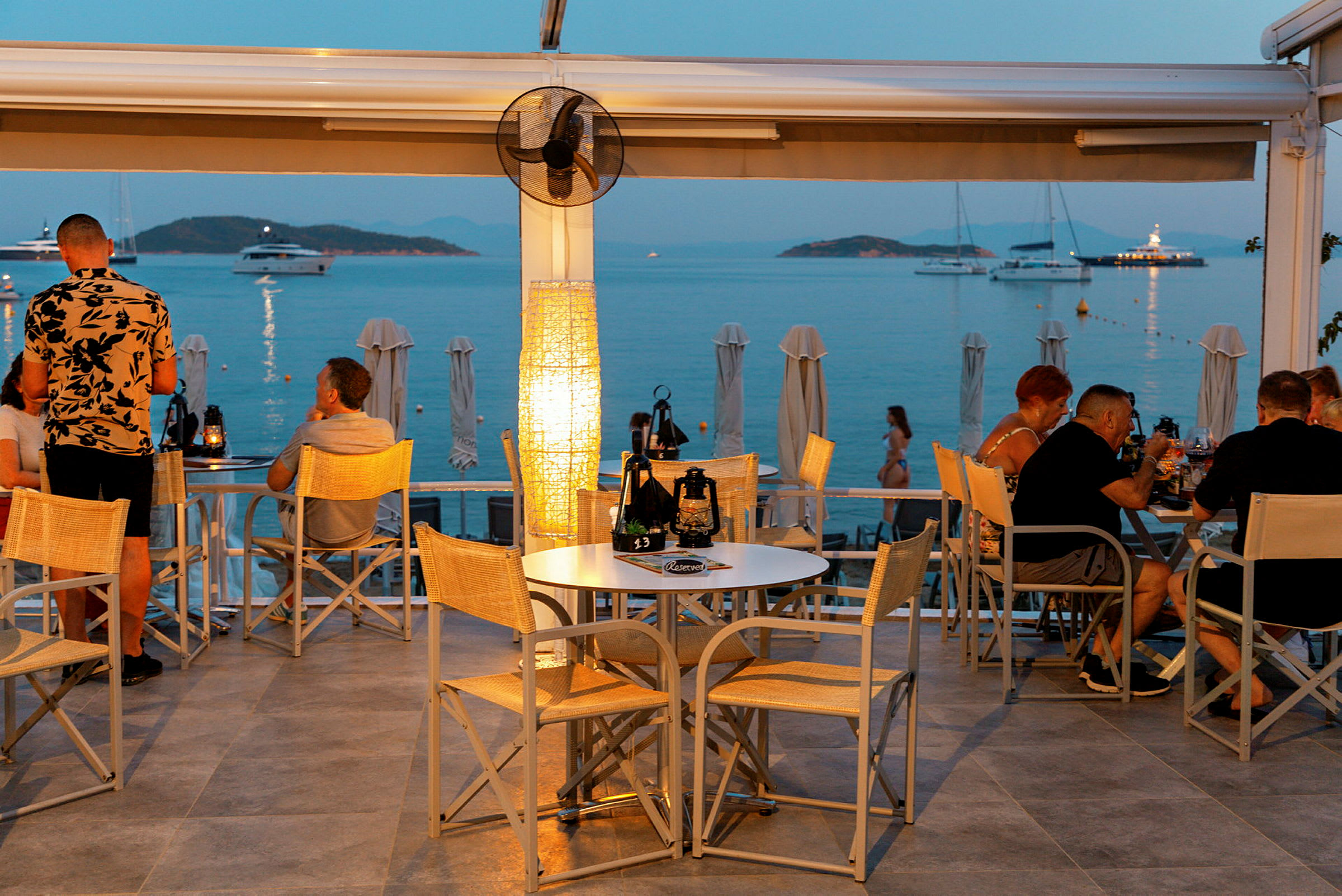 En restaurant med utsikt over havet og båter ved solnedgang. (AI-generert tekst)
