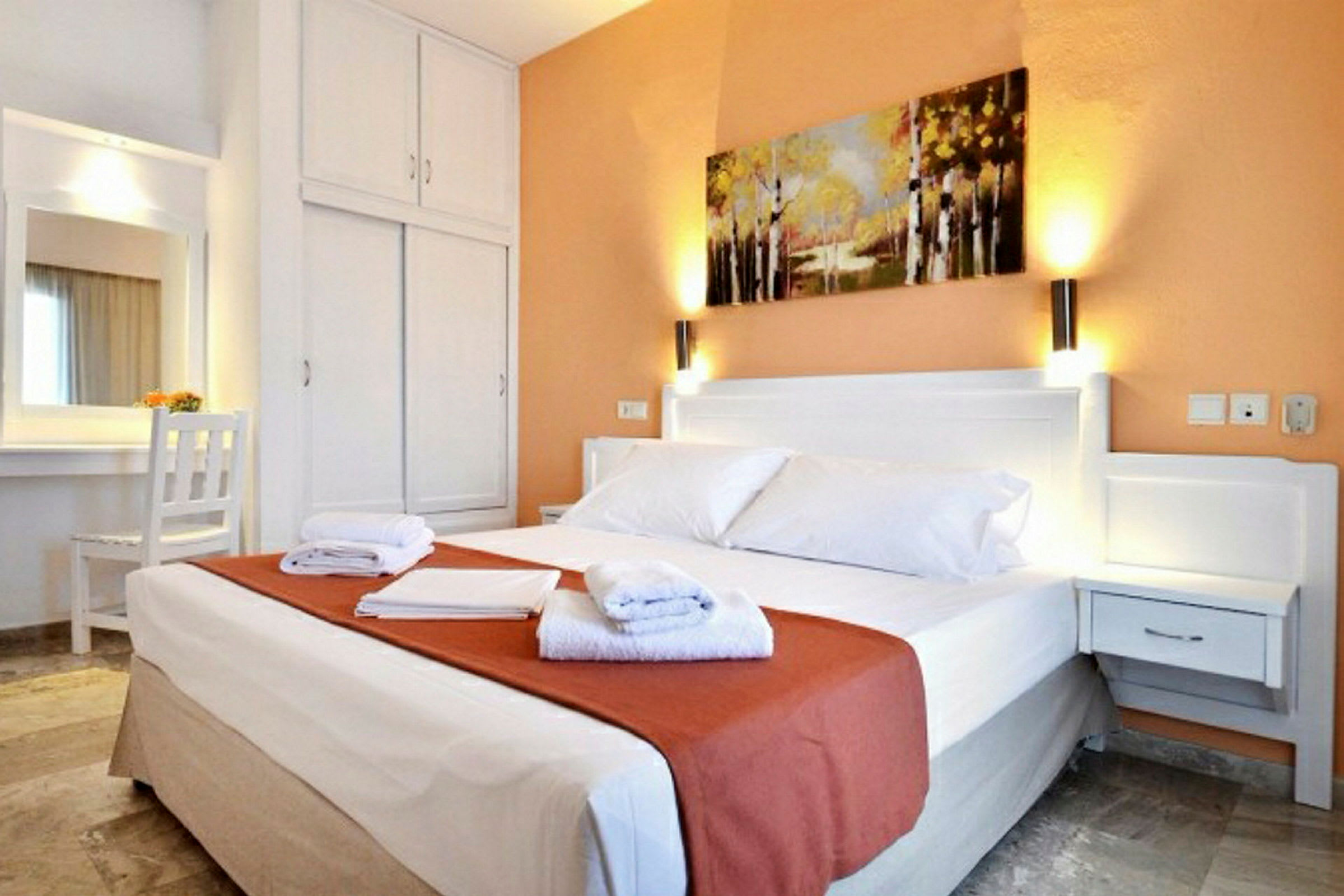 Hotellrom med en dobbeltseng, nattbord, garderobe og et maleri på veggen. (AI-generert tekst)