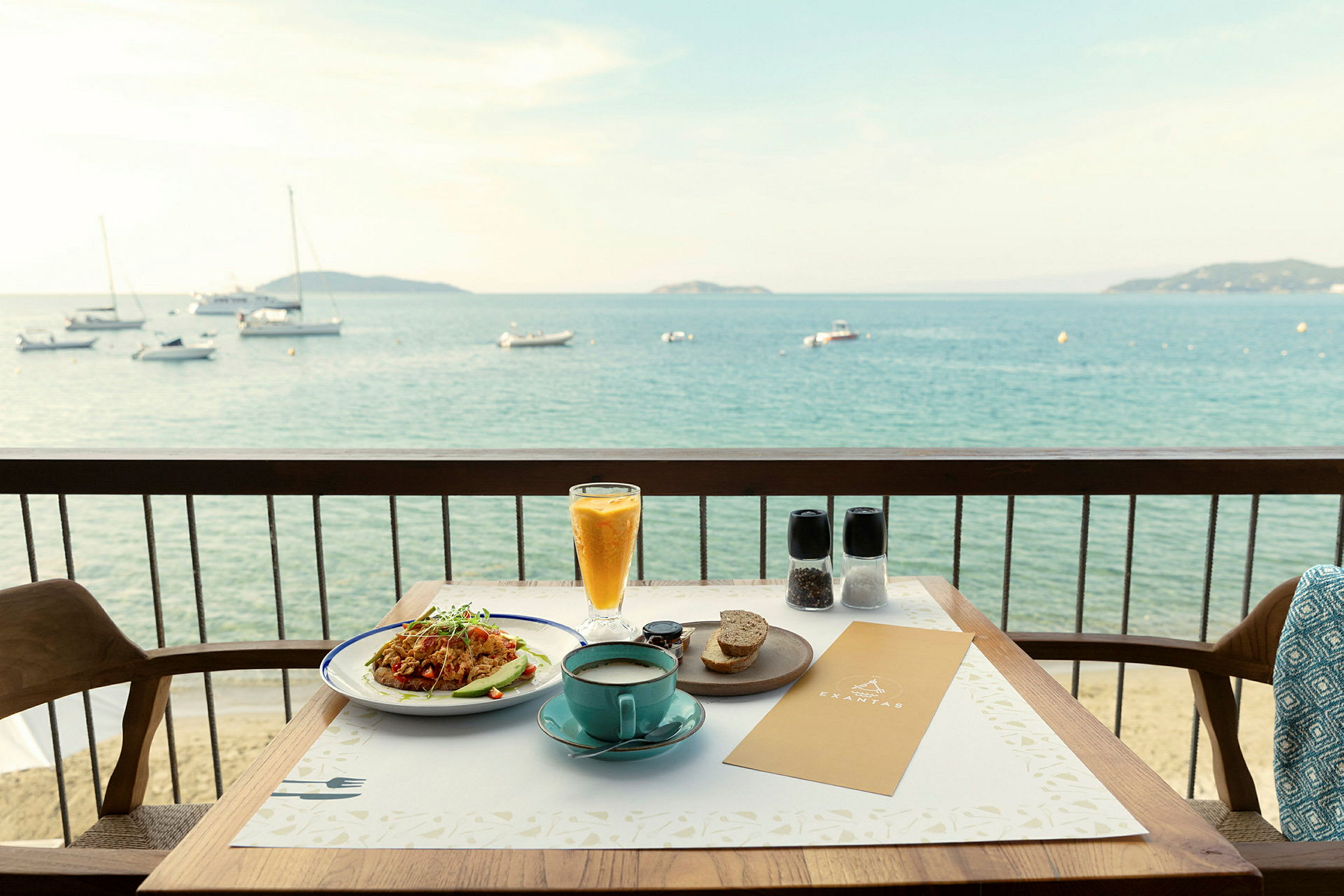 Utsikt over en tallerken med mat og en kopp kaffe plassert på et bord på en balkong med utsikt over havet. (AI-generert tekst)