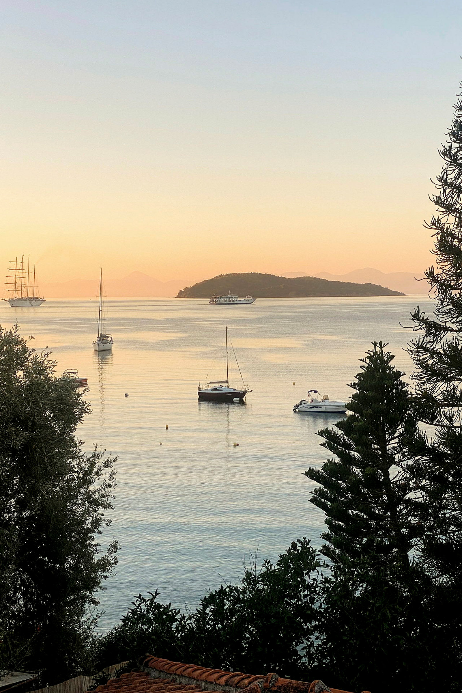 Båter ligger fortøyd ved en stille havutsikt med en øy i bakgrunnen. (AI-generert tekst)