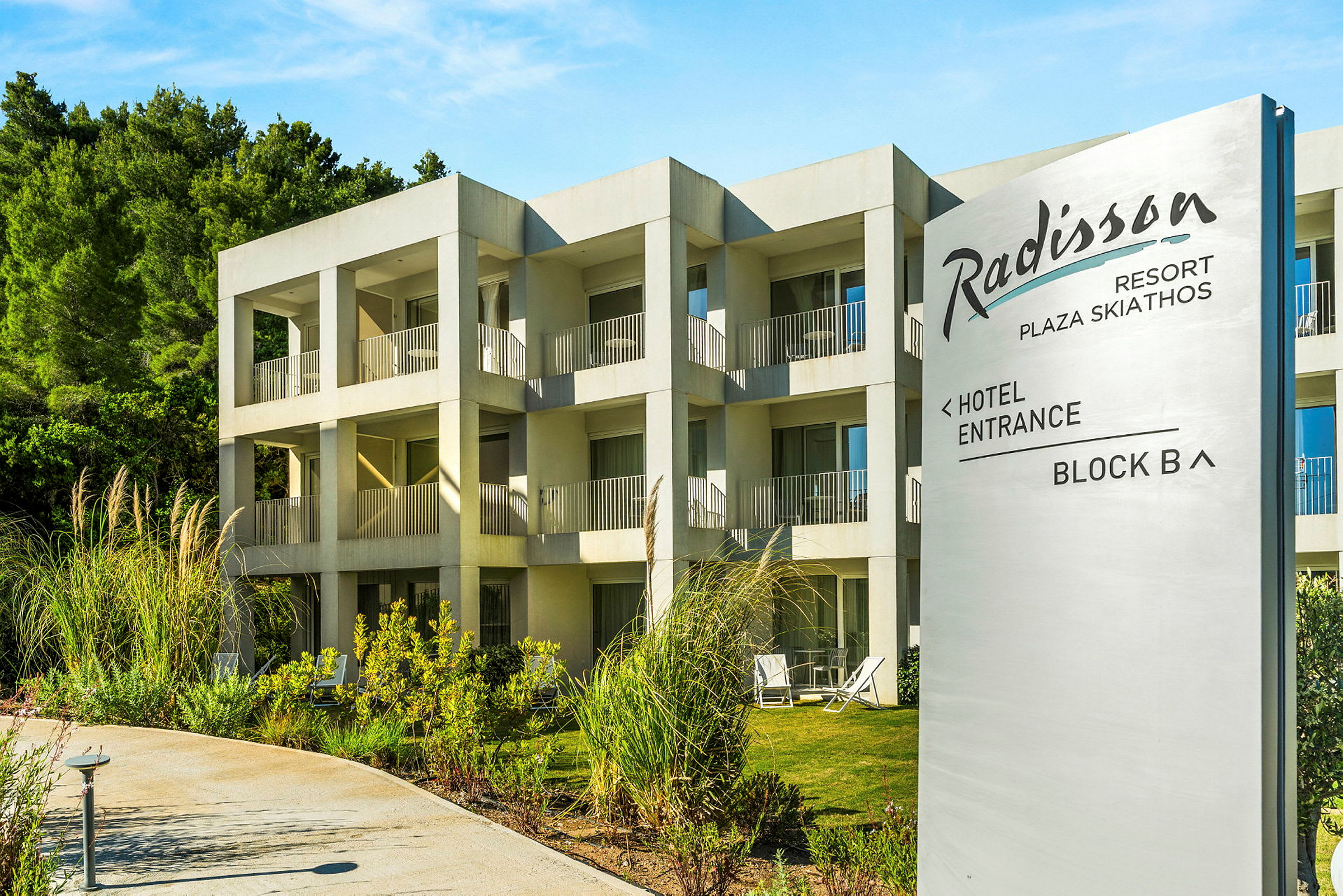 Hotelbygning med flere rom og balkonger, med et skilt som viser Radisson Resort Plaza Skiathos. (AI-generert tekst)