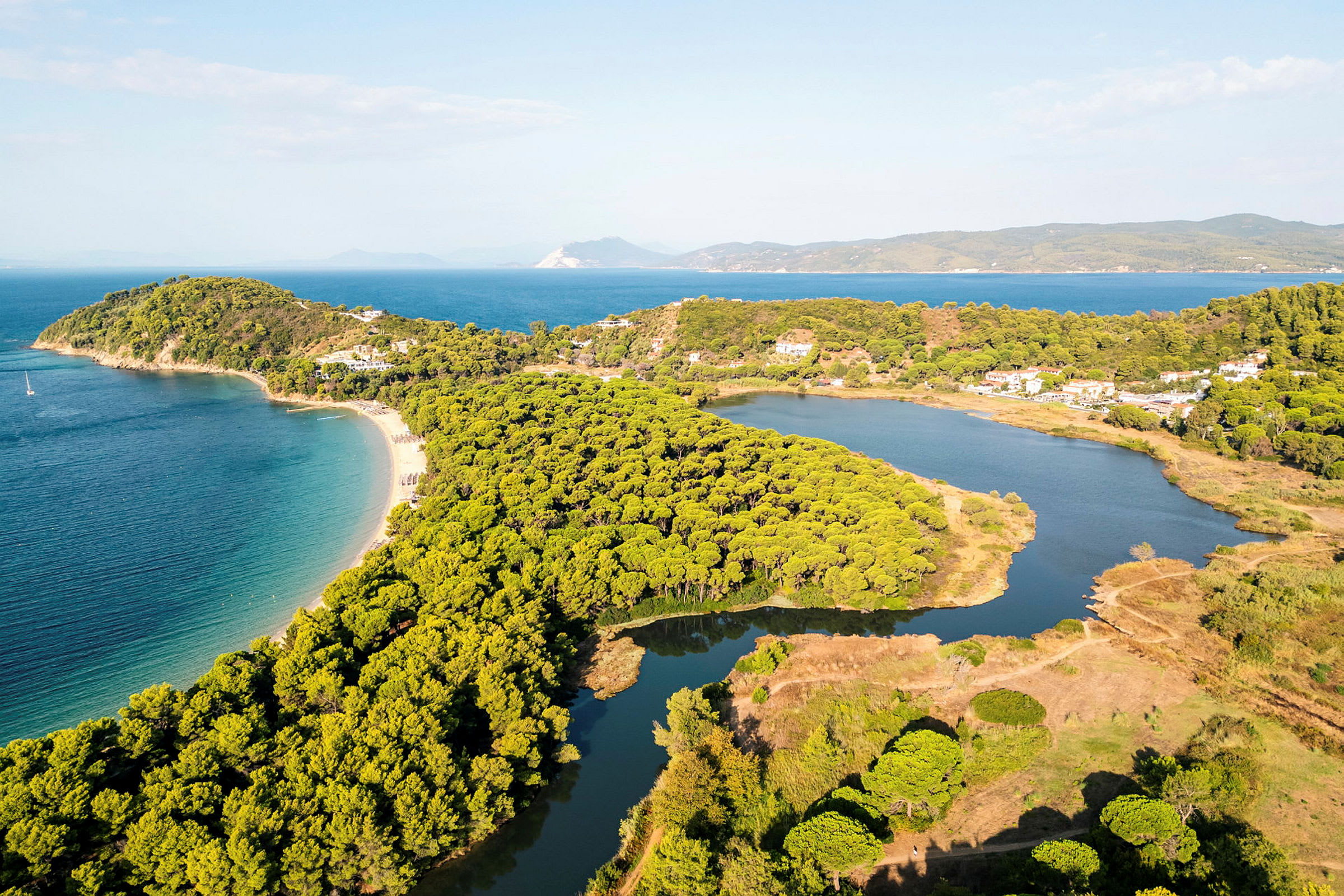Flyfoto av en kystlinje med sandstrand, frodig skog og rolig vann. (AI-generert tekst)