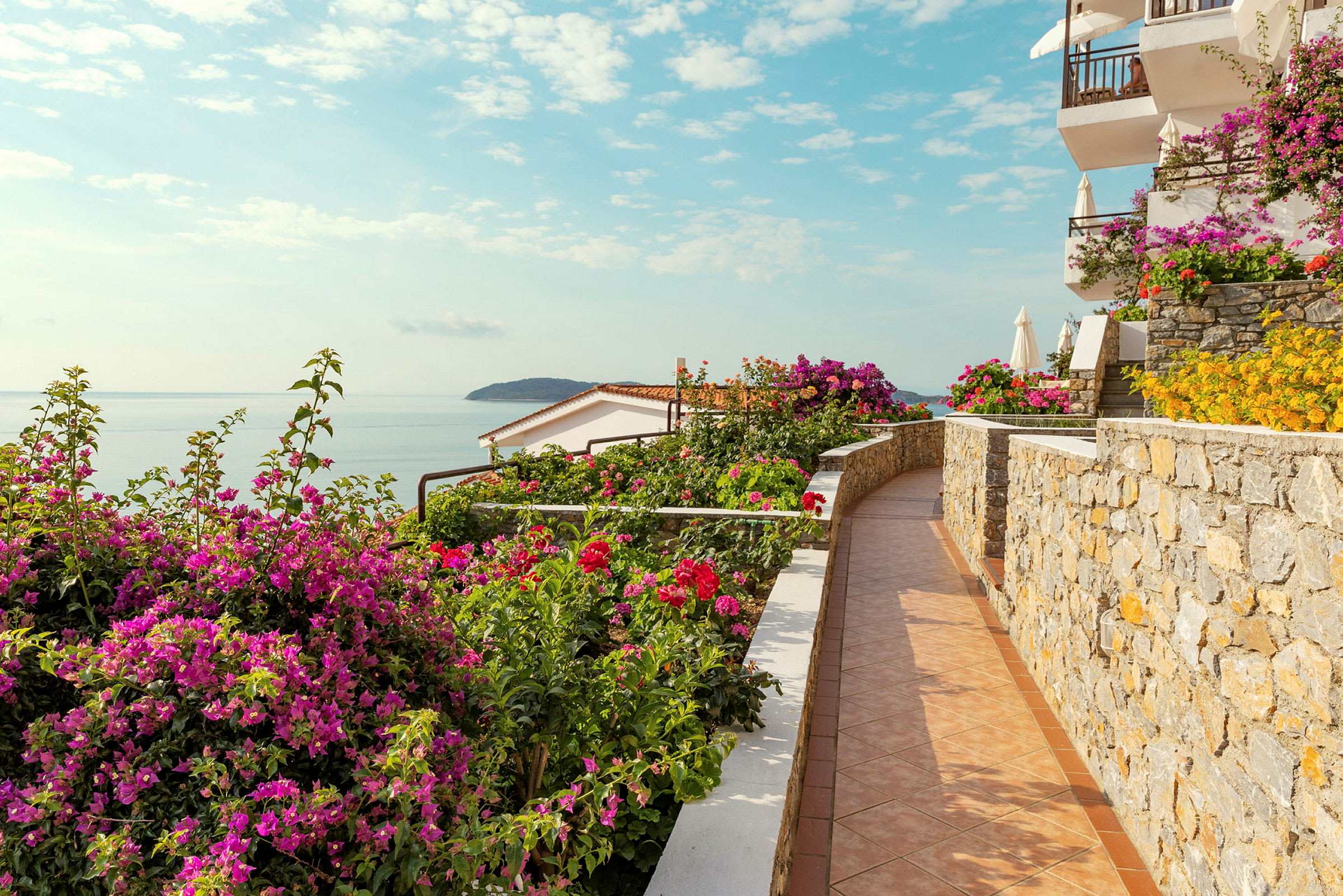 En steinmur med blomstrende planter og havet i bakgrunnen. (AI-generert tekst)