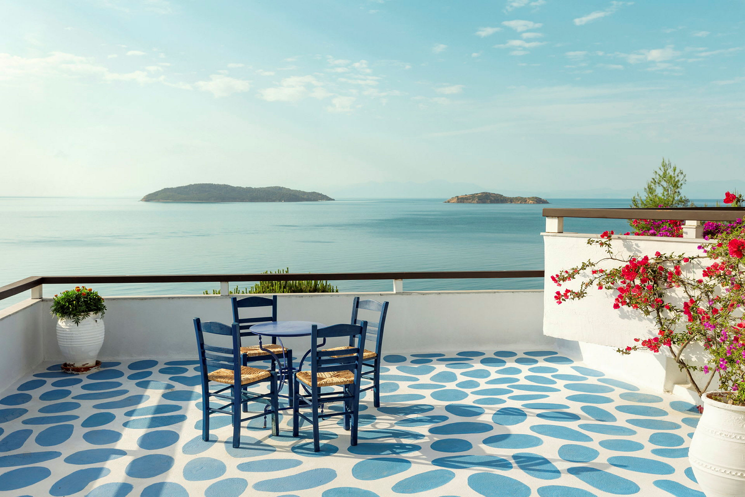 Utsikt over havet fra en terrasse med et bord og stoler. (AI-generert tekst)