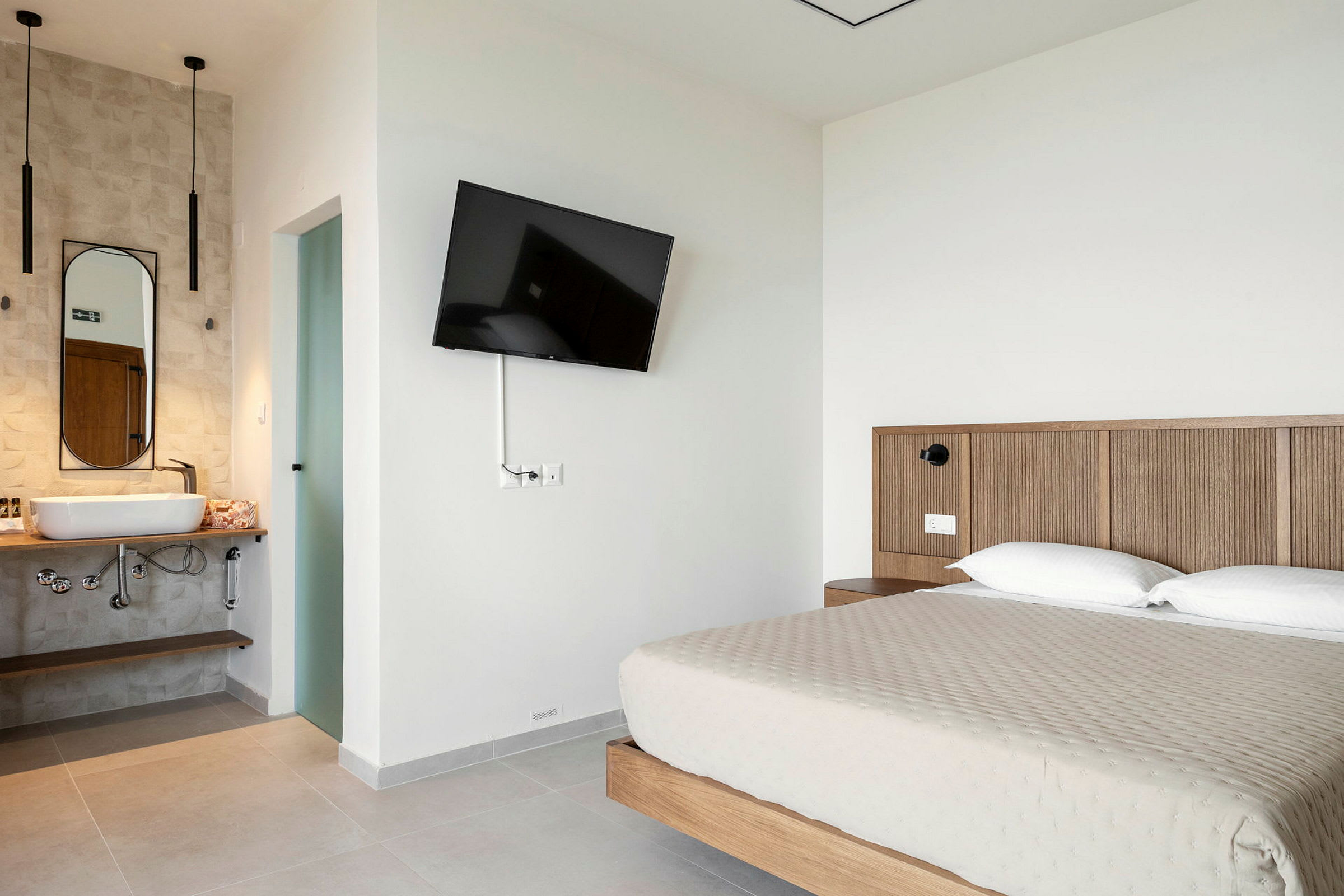Hotellrom med en dobbeltseng, veggmontert TV og et åpent baderom. (AI-generert tekst)