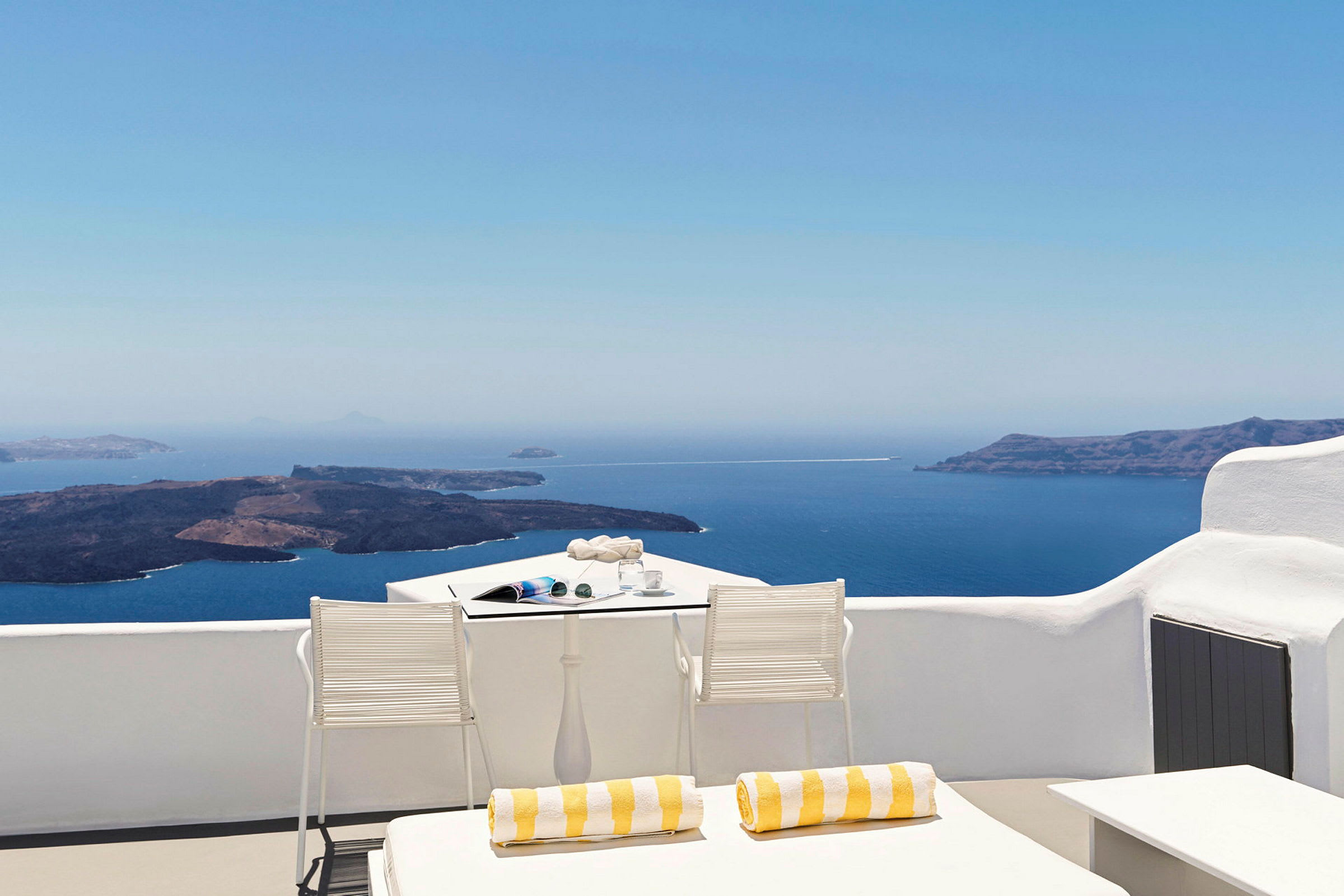 Hvit terrasse med utsikt over havet og øyer, med solsenger og et bord med stoler. (AI-generert tekst)