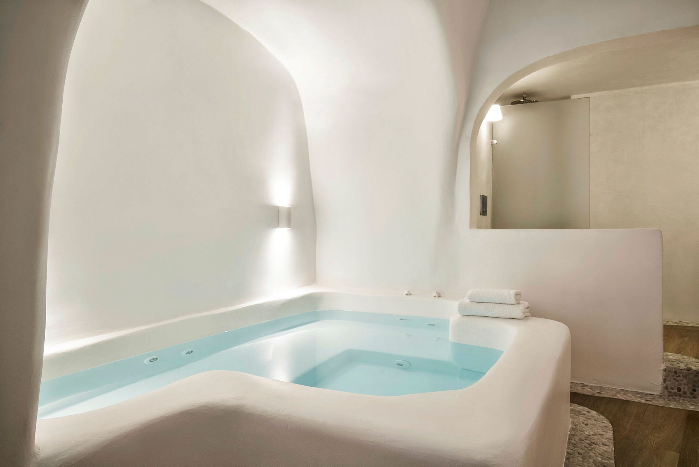 Et lite innendørs spa med hvite fliser og blått vann i lyst miljø. (AI-generert tekst)