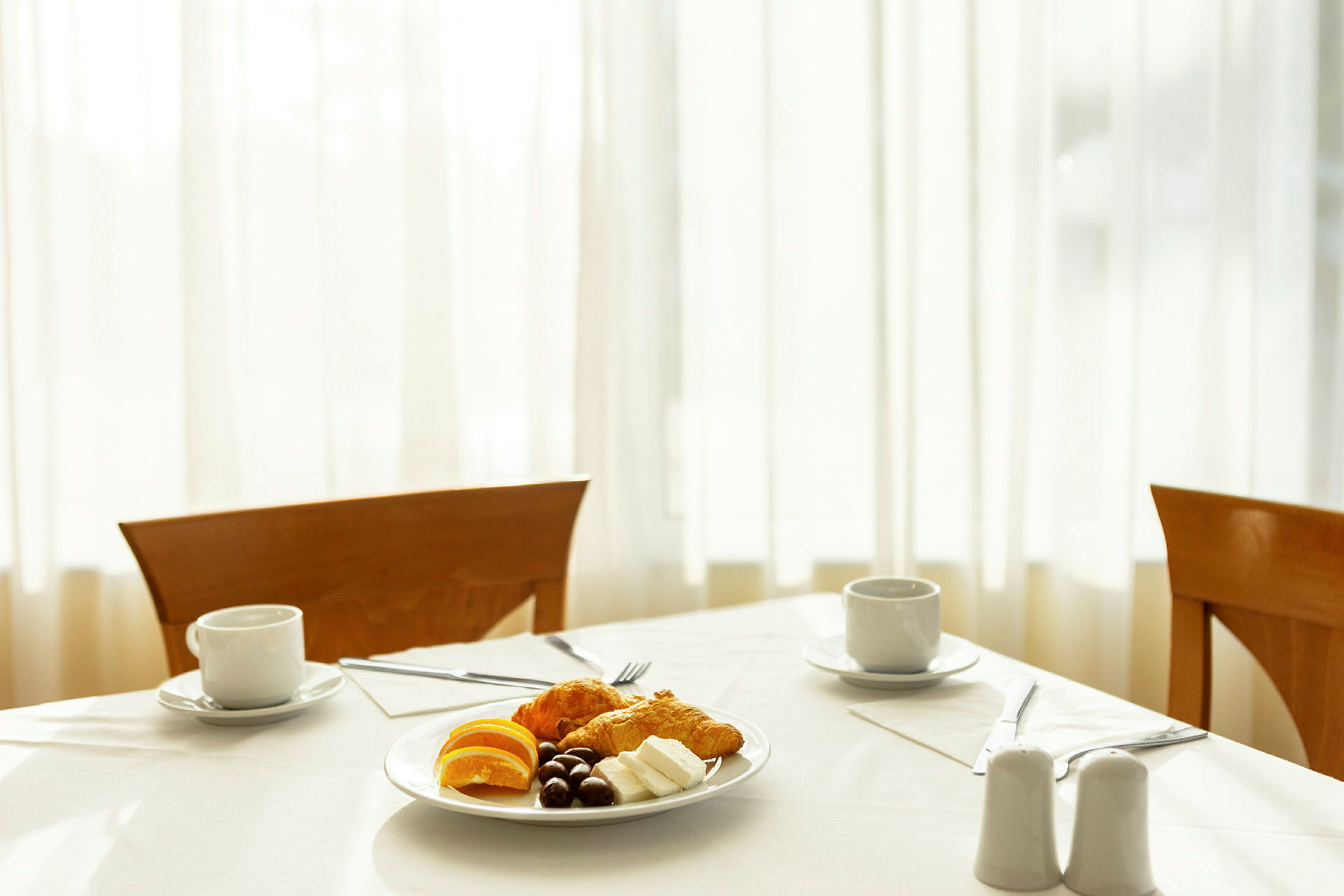 En oppdekket frokost med en tallerken som inneholder croissanter, appelsinskiver, ost og sjokolade samt to kopper kaffe. (AI-generert tekst)