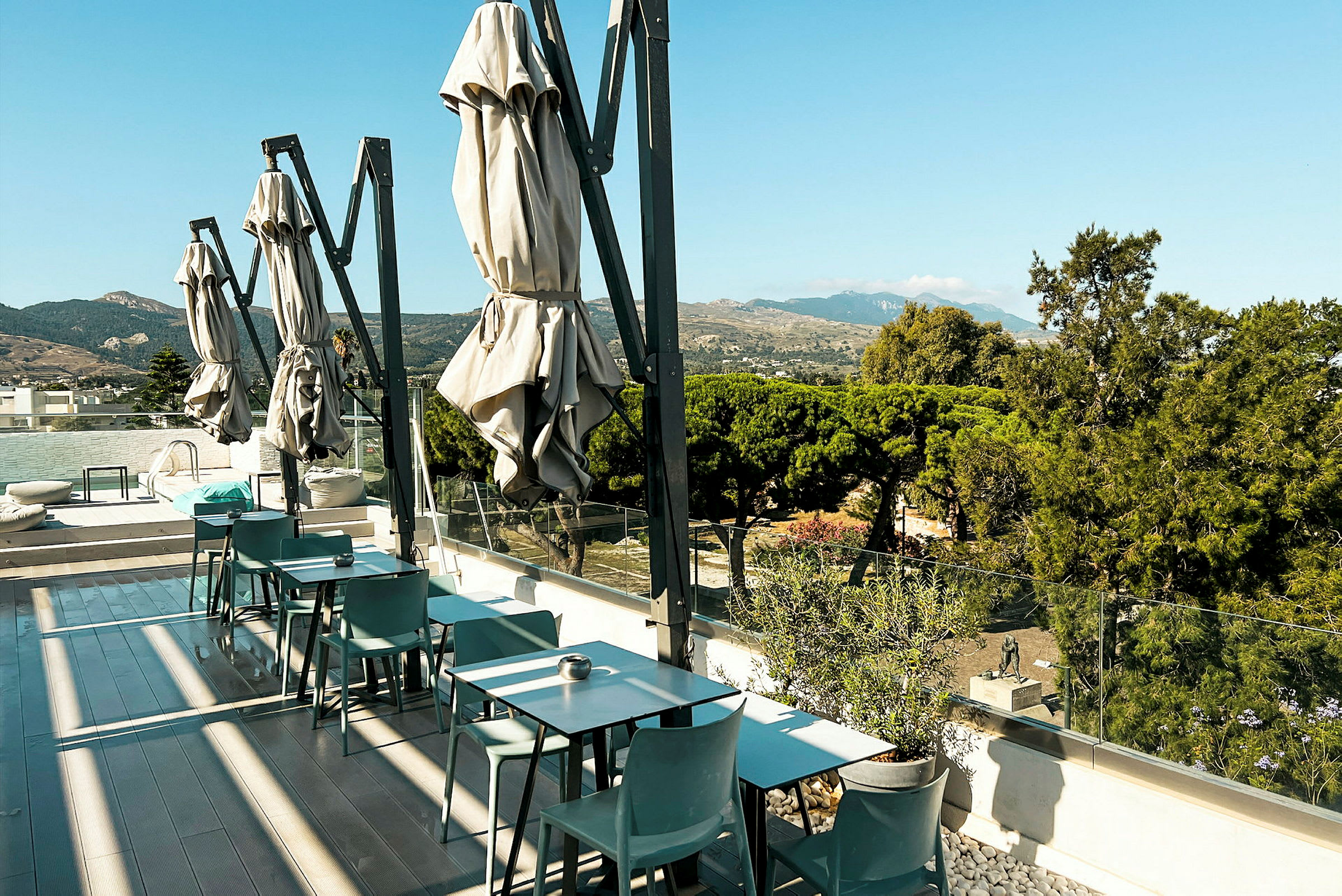 Terrasse med bord og stoler, parasoller og utsikt over grøntområder og fjell. (AI-generert tekst)