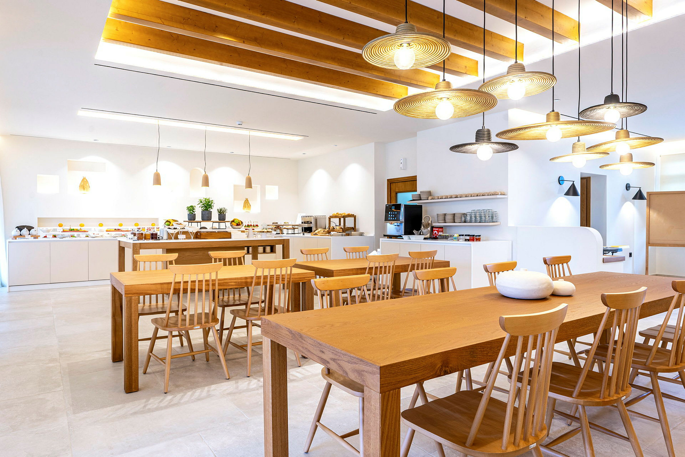 Et luftig og lyst rom med spisebord og trestoler samt en buffet på langbord i bakgrunnen. (AI-generert tekst)