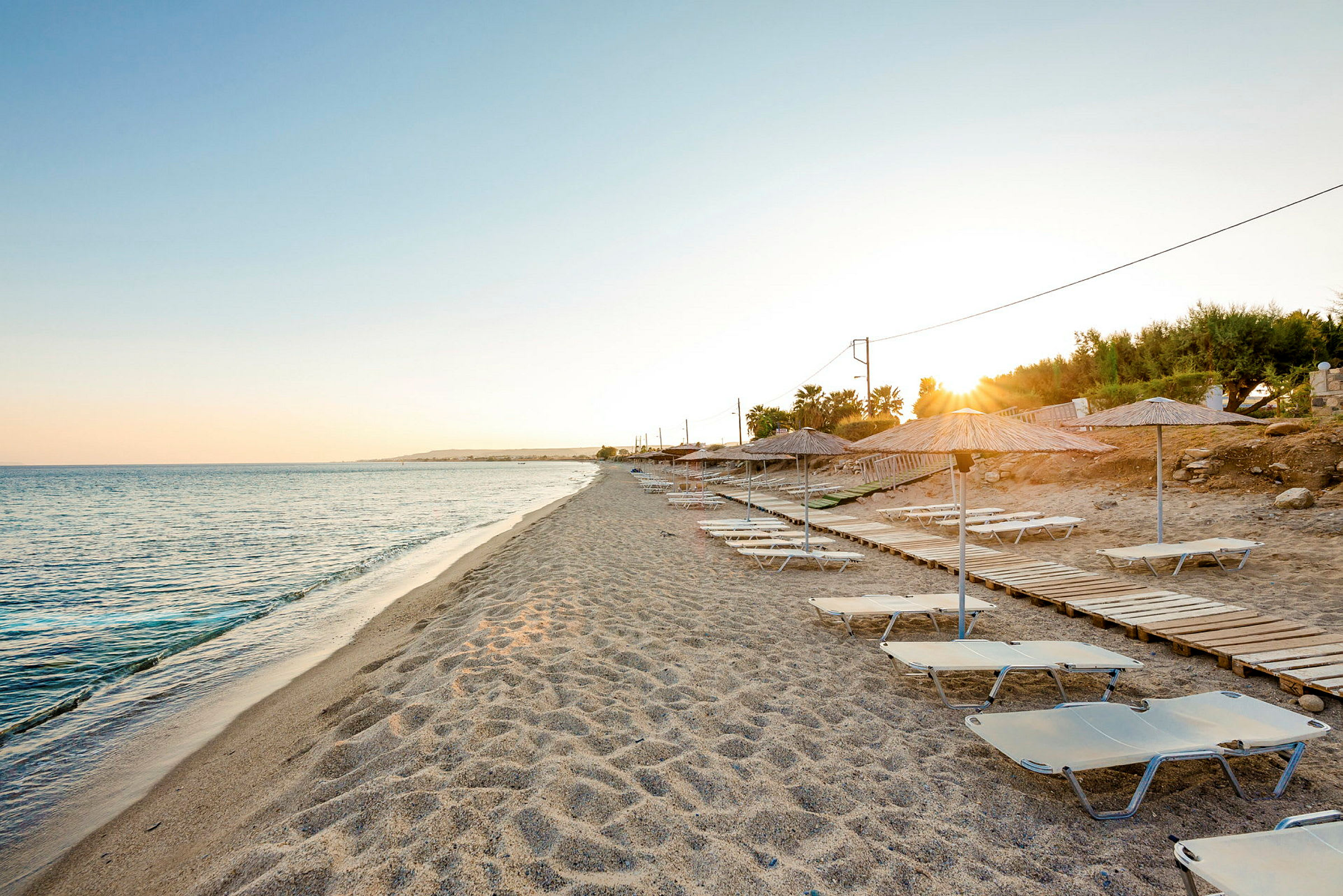 Strand med solsenger og parasoller ved solnedgang. (AI-generert tekst)