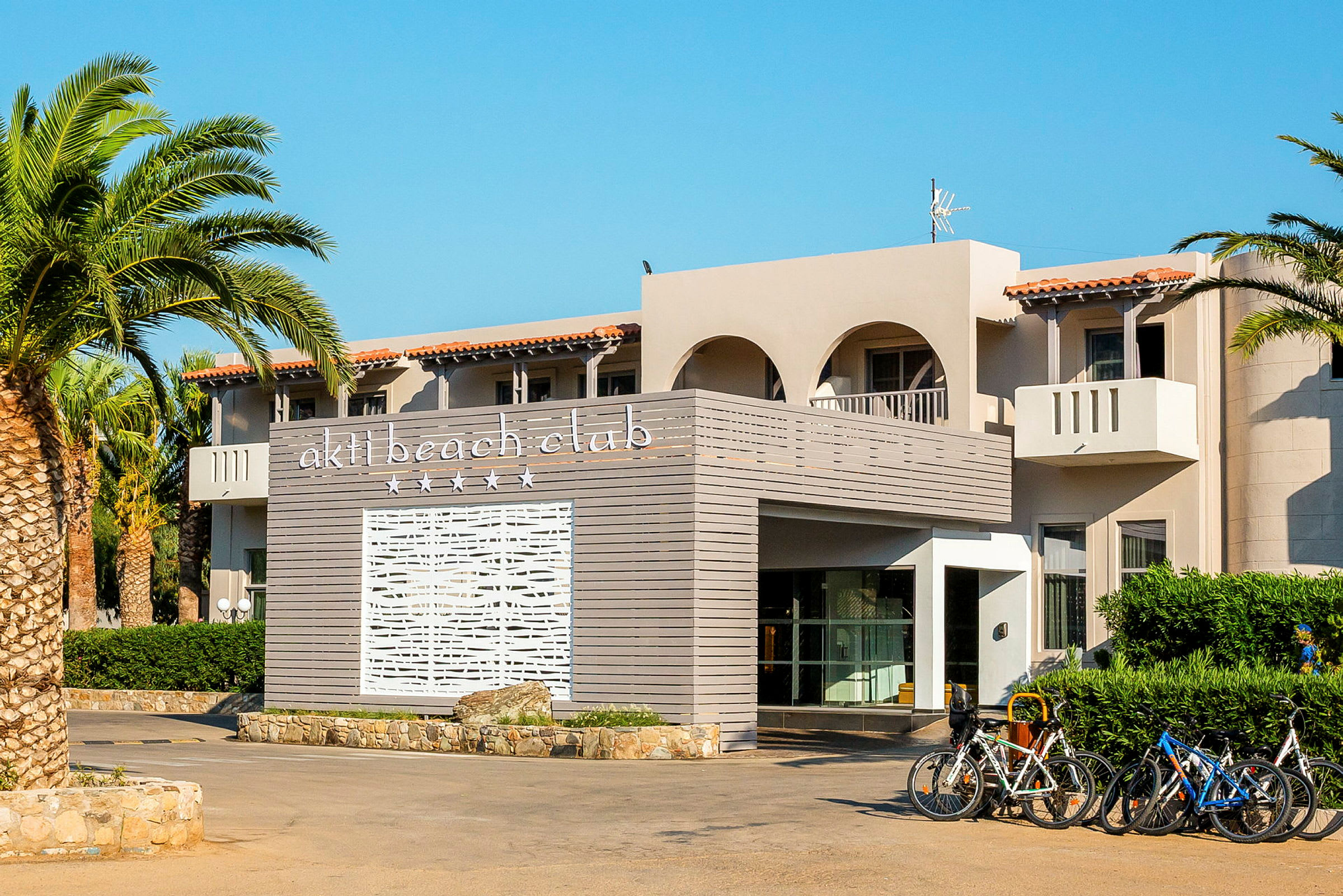 Bygning med teksten 'akti beach club' på en panel i forgrunnen og sykler parkert ved inngangen. (AI-generert tekst)