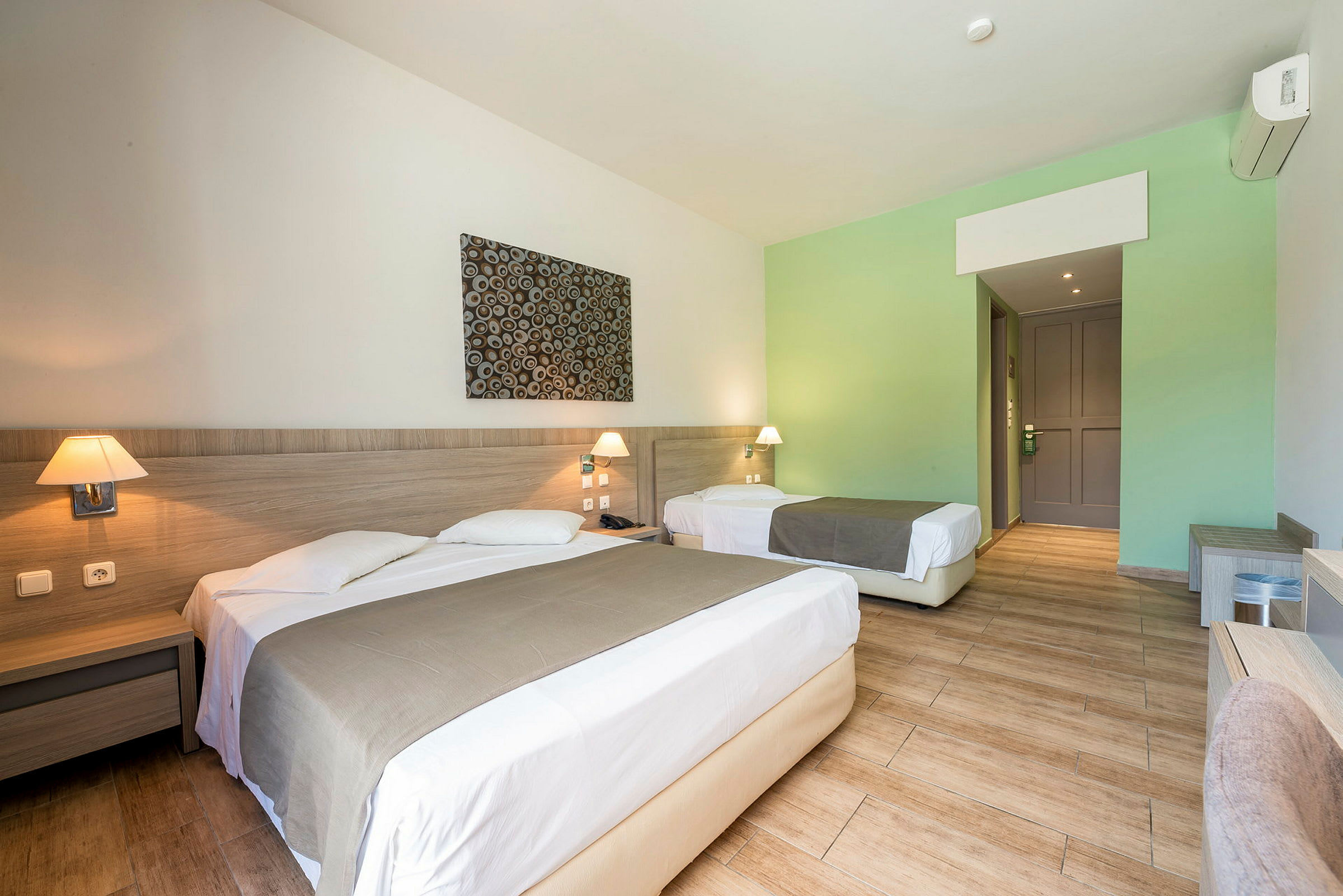 Hotellrom med en dobbeltseng og en enkeltseng, begge med sengetepper og nattbord. (AI-generert tekst)