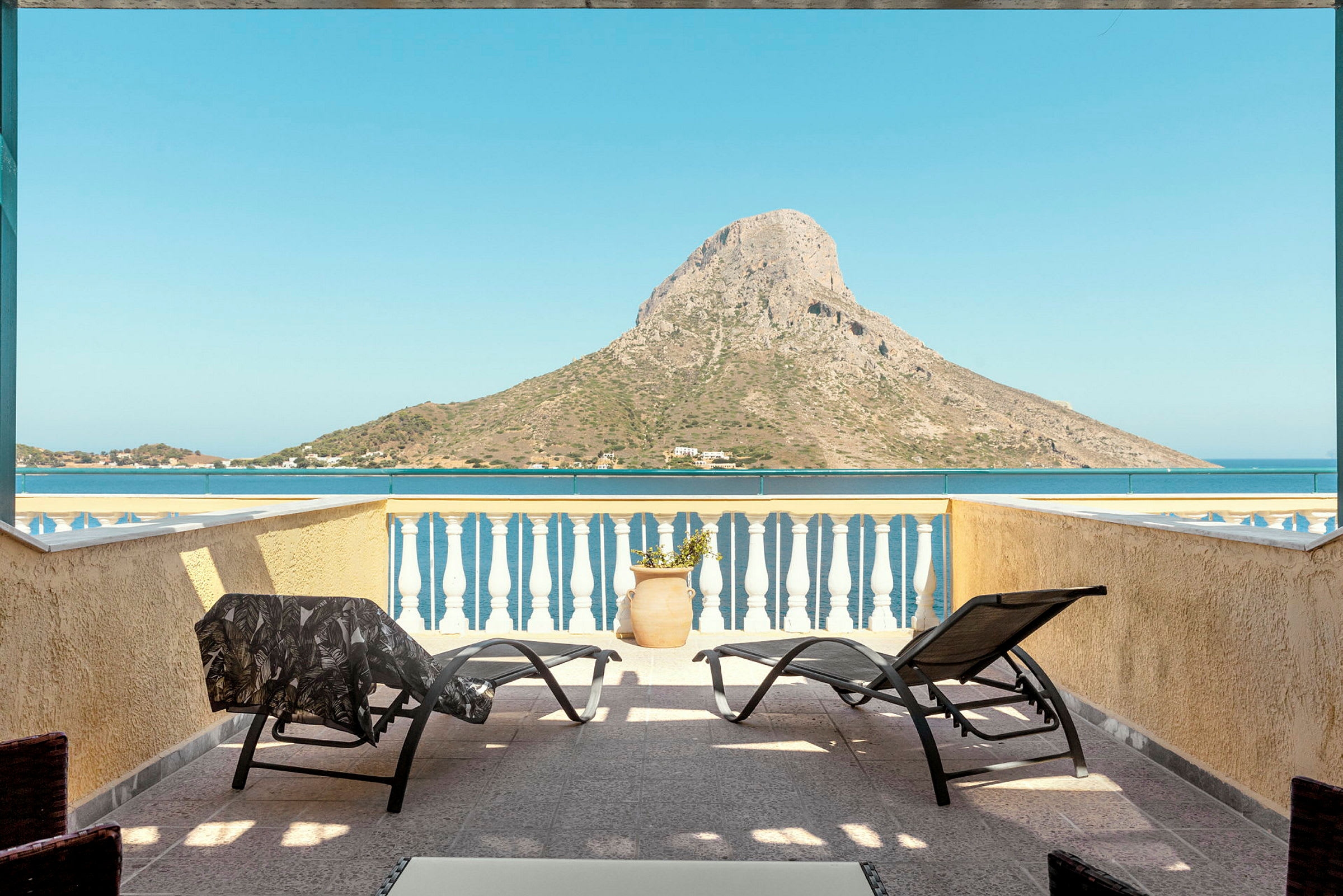 En terrasse med solsenger og utsikt over havet og en fjellformasjon. (AI-generert tekst)