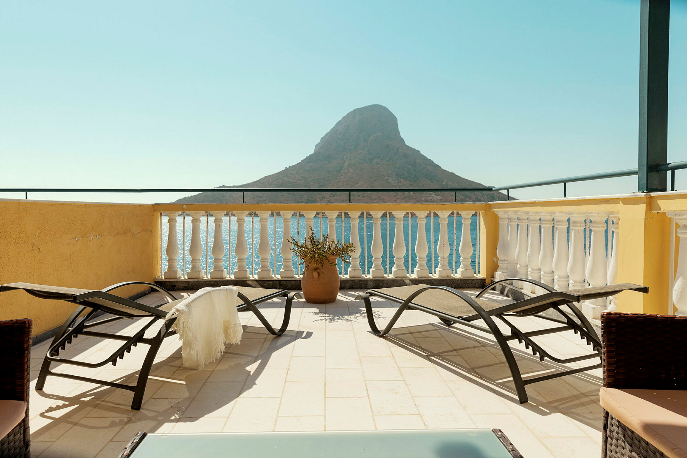 Terrasse med solsenger og utsikt over havet og en liten fjellformasjon. (AI-generert tekst)