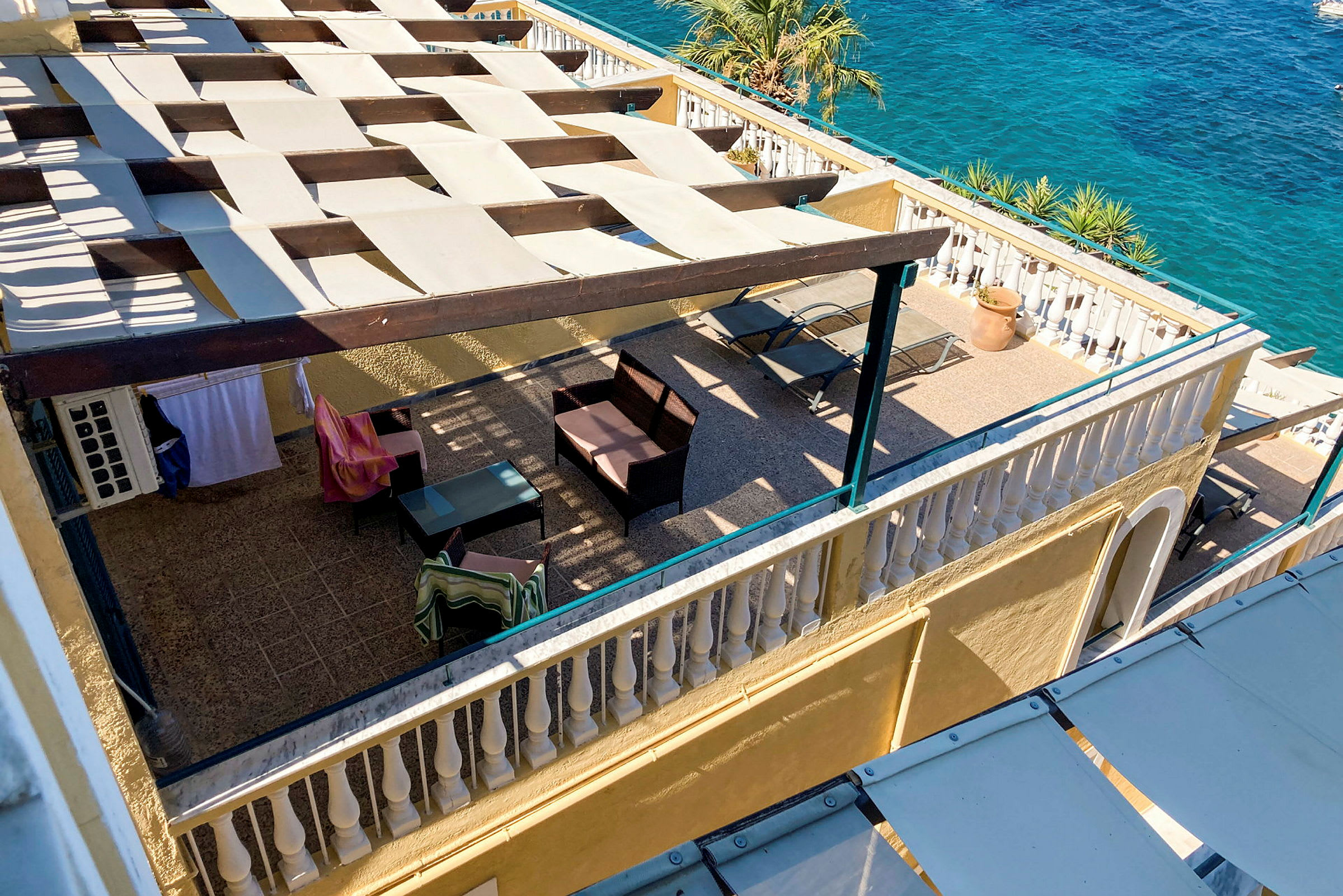 En utsikt over en terrasse med skyggende pergola, møbler og utsikt mot havet. (AI-generert tekst)