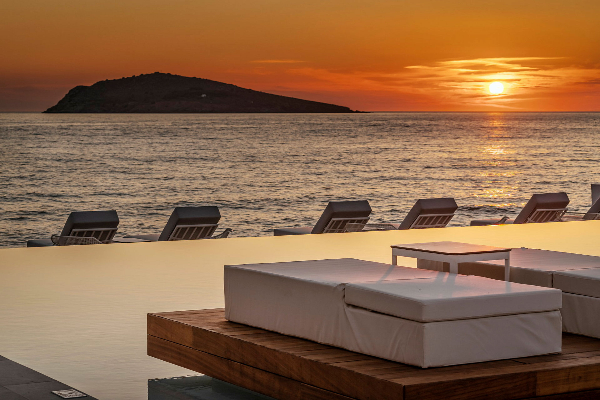 Solnedgang over havet med solsenger ved et infinity-basseng. (AI-generert tekst)
