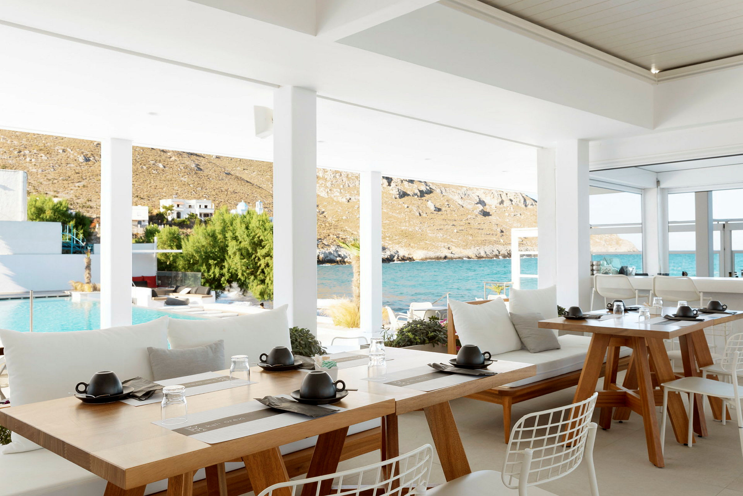 En åpen restaurant med utsikt over et basseng og havet i bakgrunnen. (AI-generert tekst)