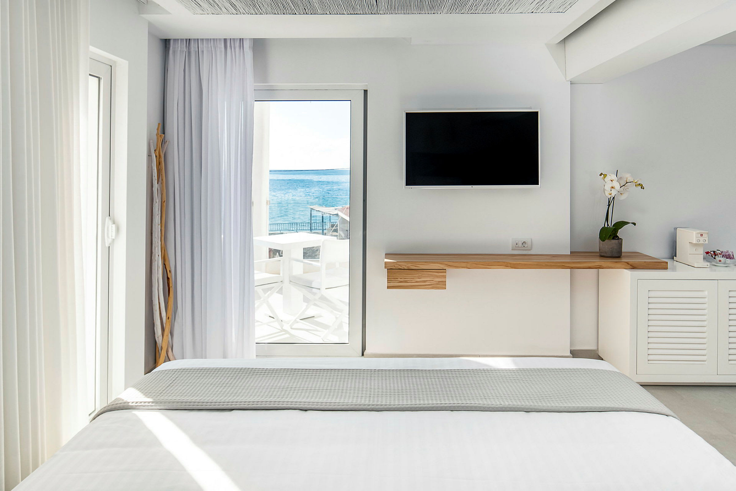Interiør av et lyst hotellrom med en seng og havutsikt gjennom en glassdør. (AI-generert tekst)