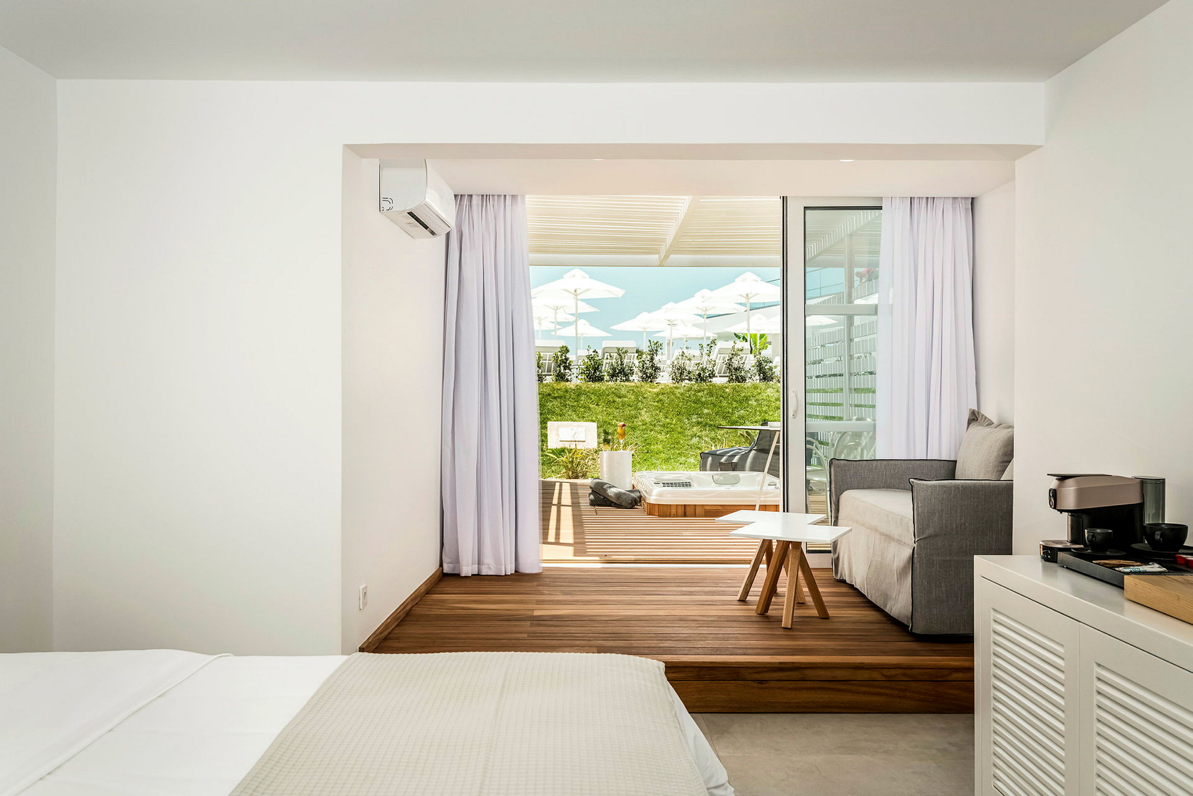 Et hotellrom med et moderne soverom og sittegruppe samt en terrasse utenfor med plen og solsenger. (AI-generert tekst)