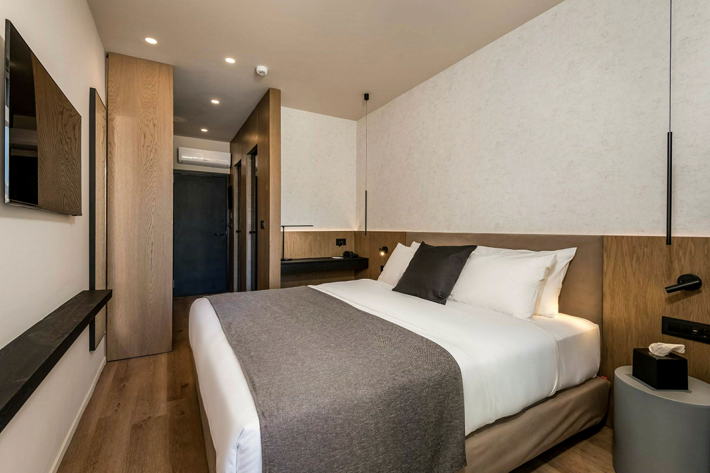Moderne hotellrom med dobbeltseng, nattbord og veggmontert TV. (AI-generert tekst)