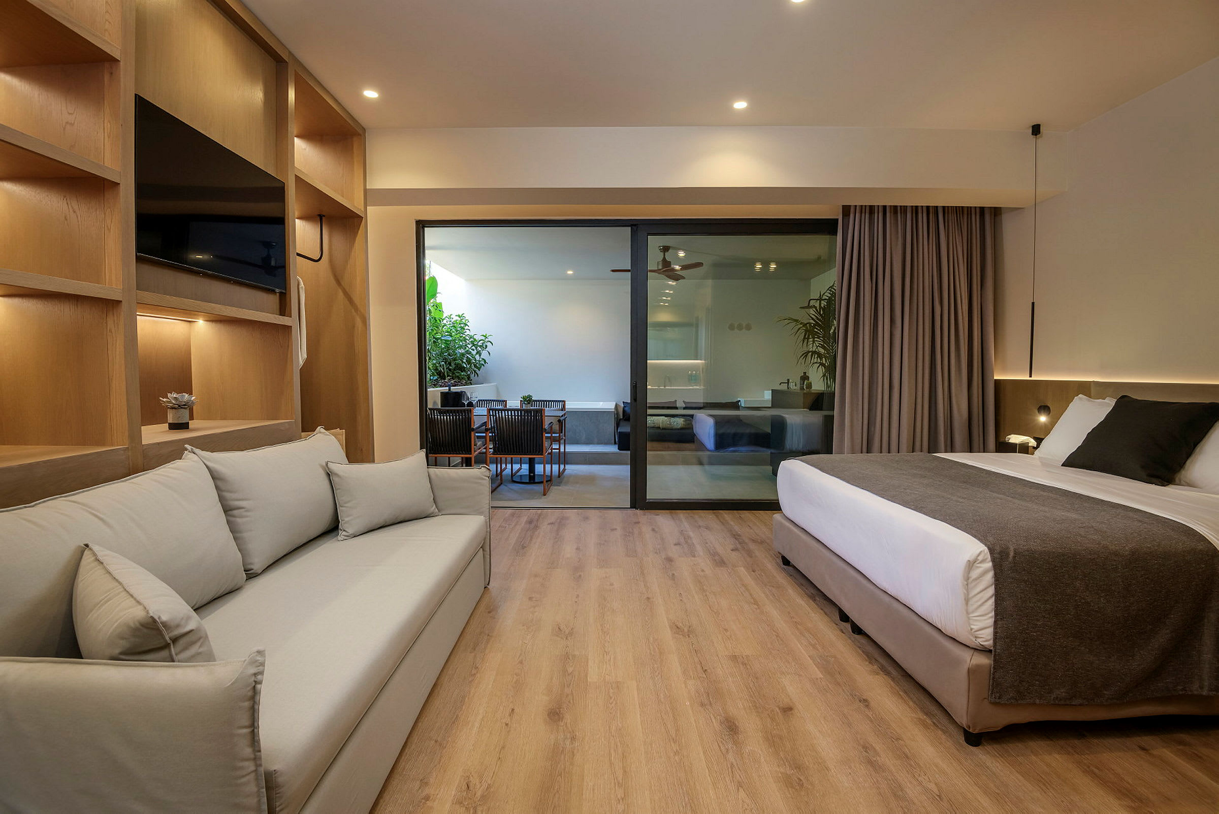 Et moderne hotellrom med sofa, seng og glassdør som leder til en sittegruppe utendørs. (AI-generert tekst)
