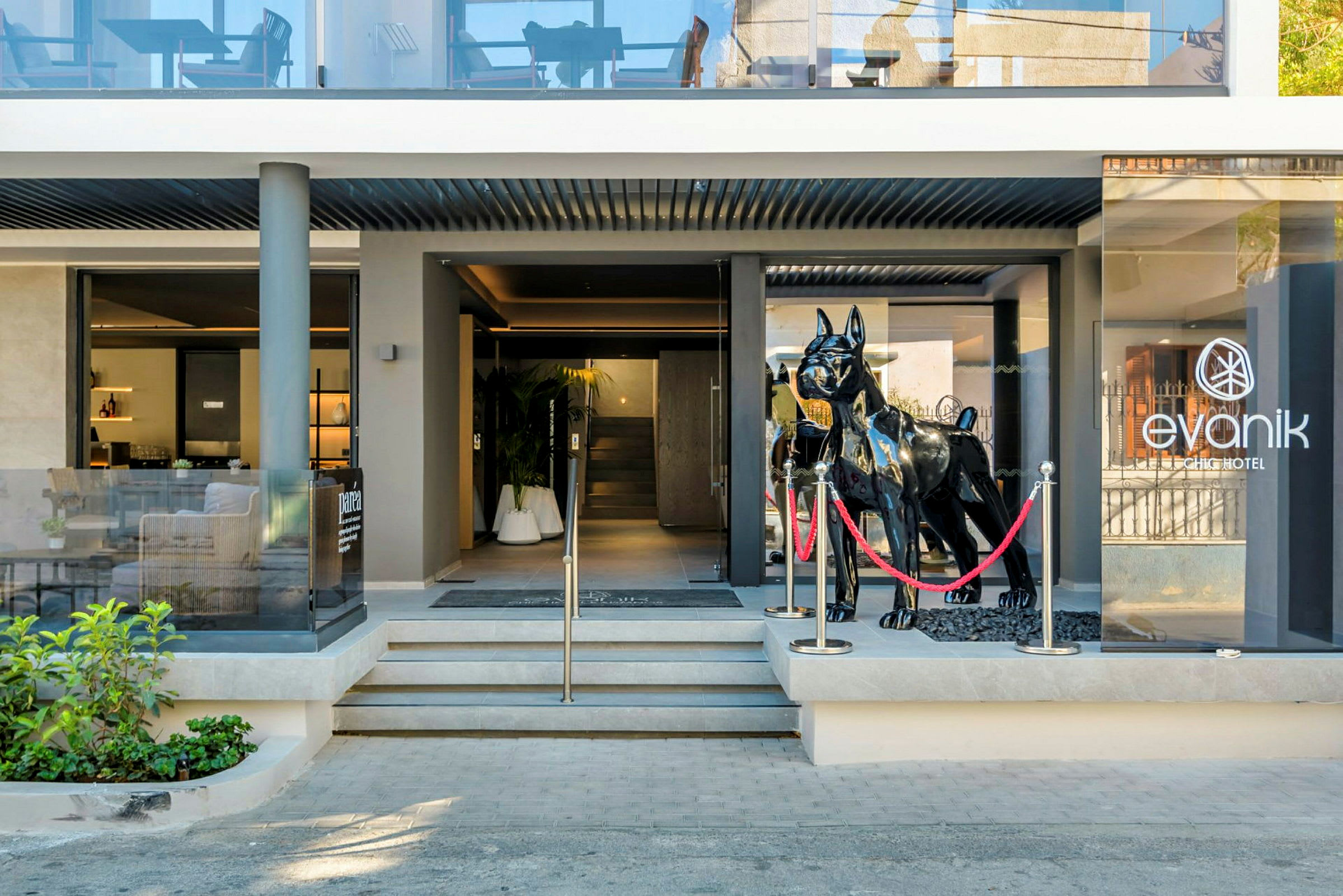 Inngangen til Evanik Chic Hotel med en stor svart skulptur av en hund foran glassdørene. (AI-generert tekst)