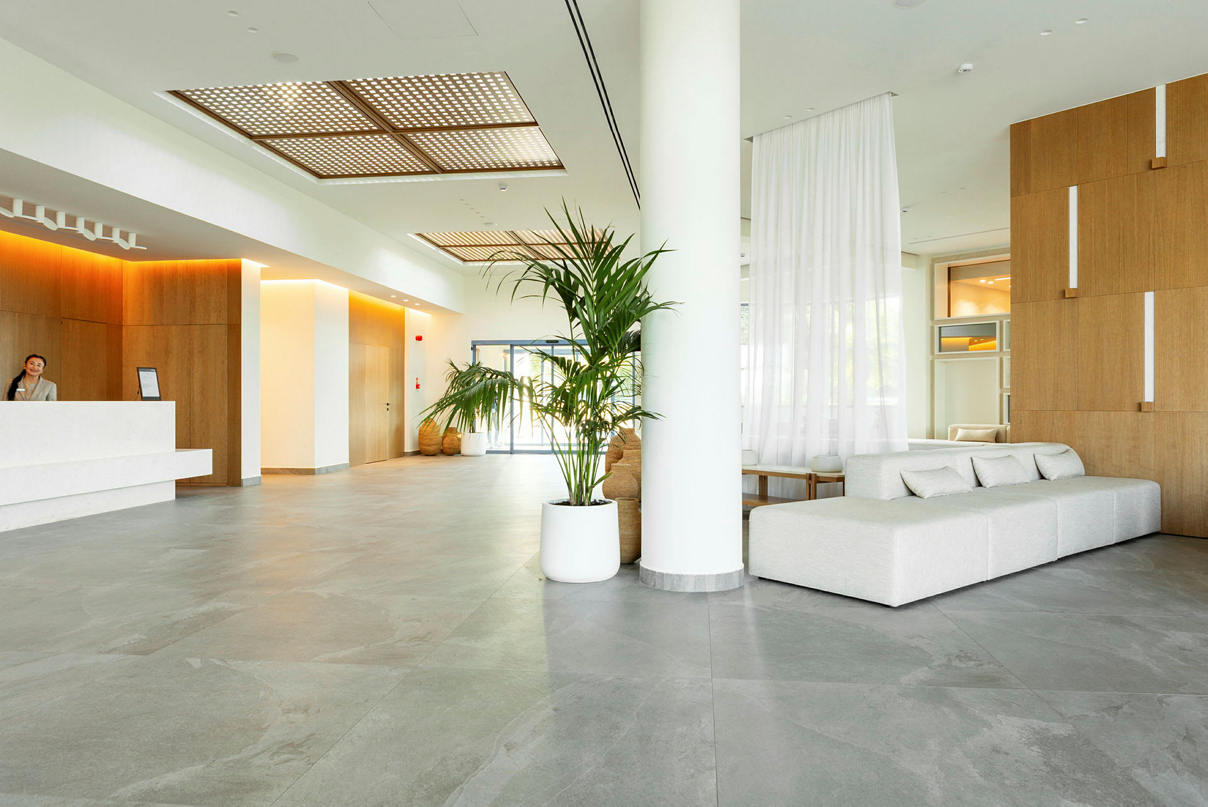 Inne i en moderne hotellobby med en resepsjon, sofaer og planter. (AI-generert tekst)