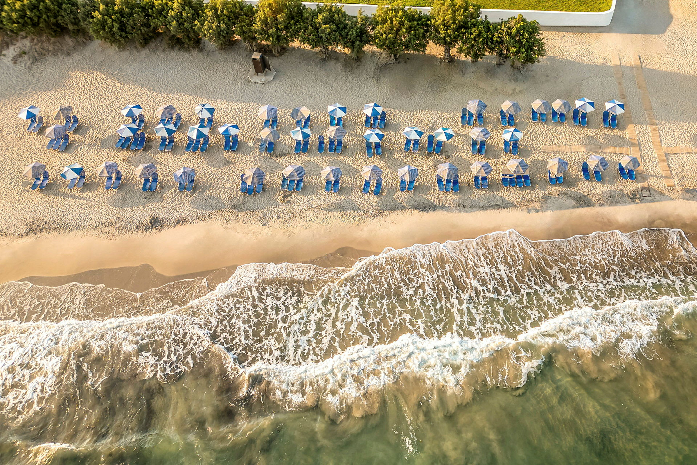 Strand med parasoller og solsenger sett ovenfra. (AI-generert tekst)
