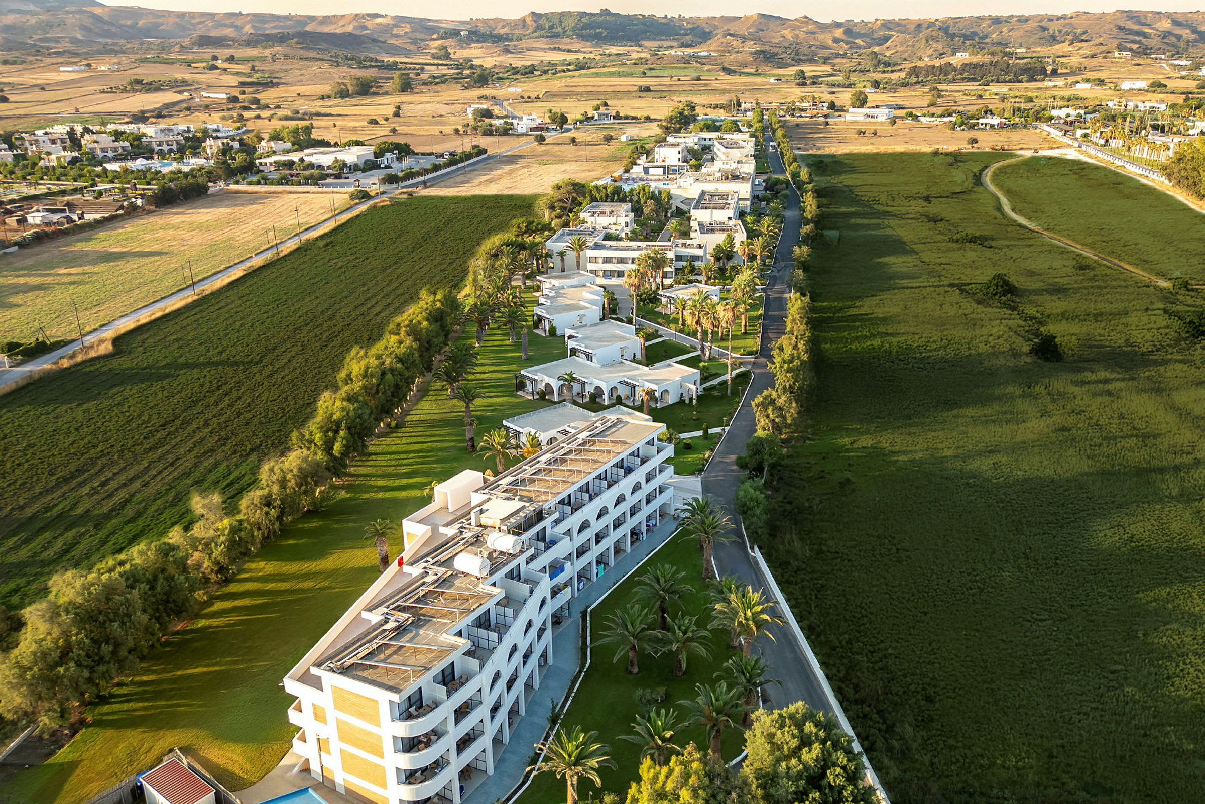 Flyfoto av et hotellkompleks omgitt av grøntområder og landskap. (AI-generert tekst)