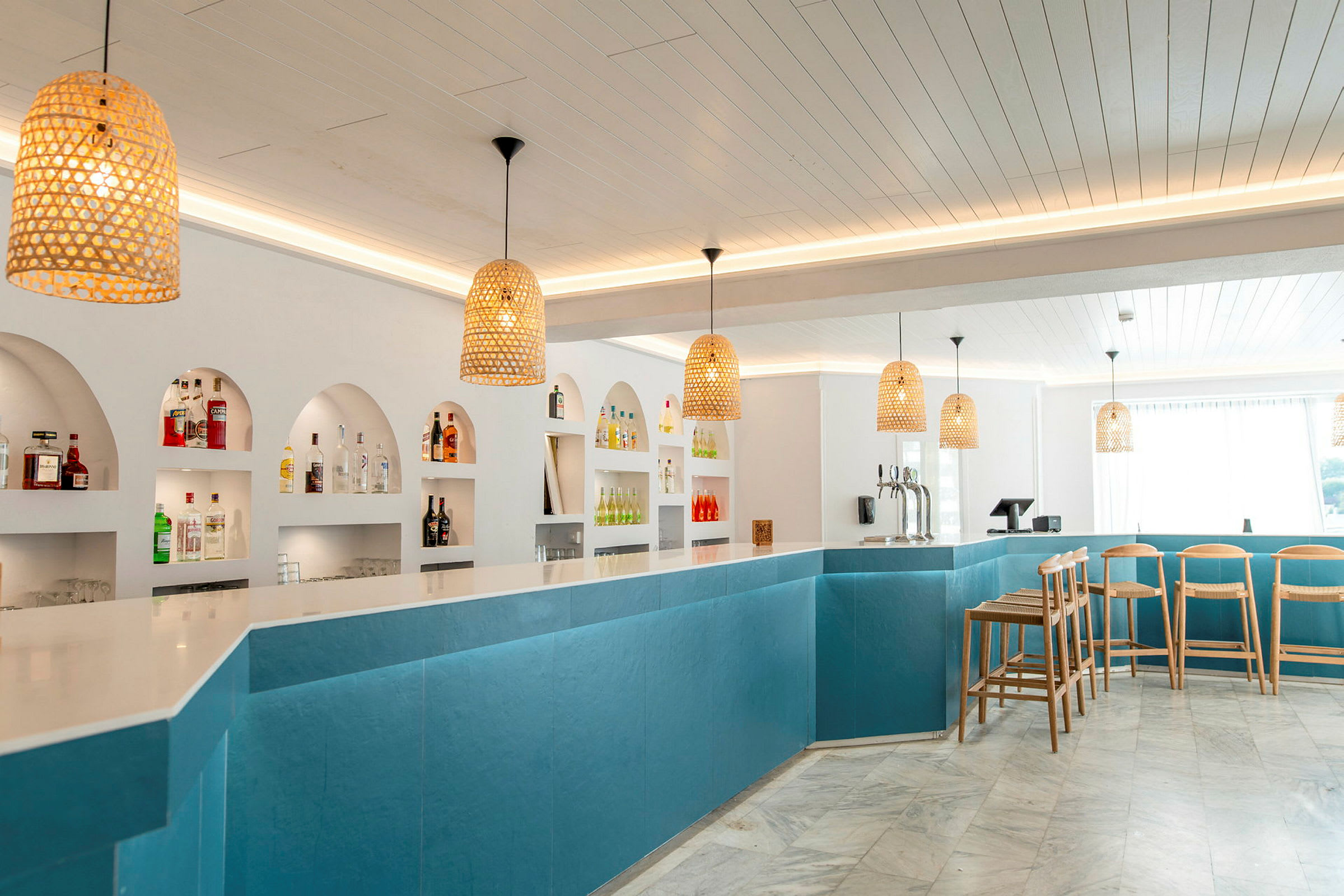 En moderne bar med blå paneler, hvit benkeplate og flere flasker på hyller bak. (AI-generert tekst)