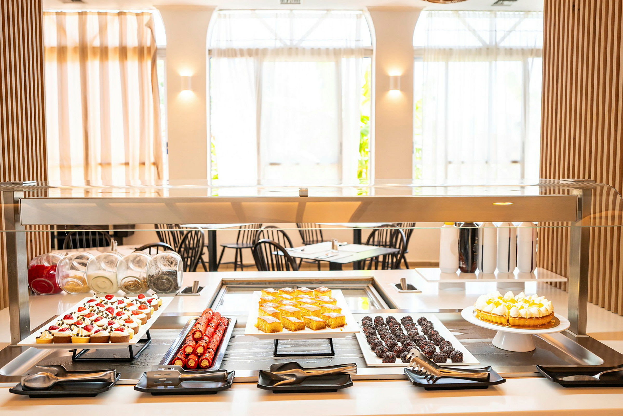 Et dessertbord med forskjellige bakverk og kaker under en glassbeskyttelse. (AI-generert tekst)