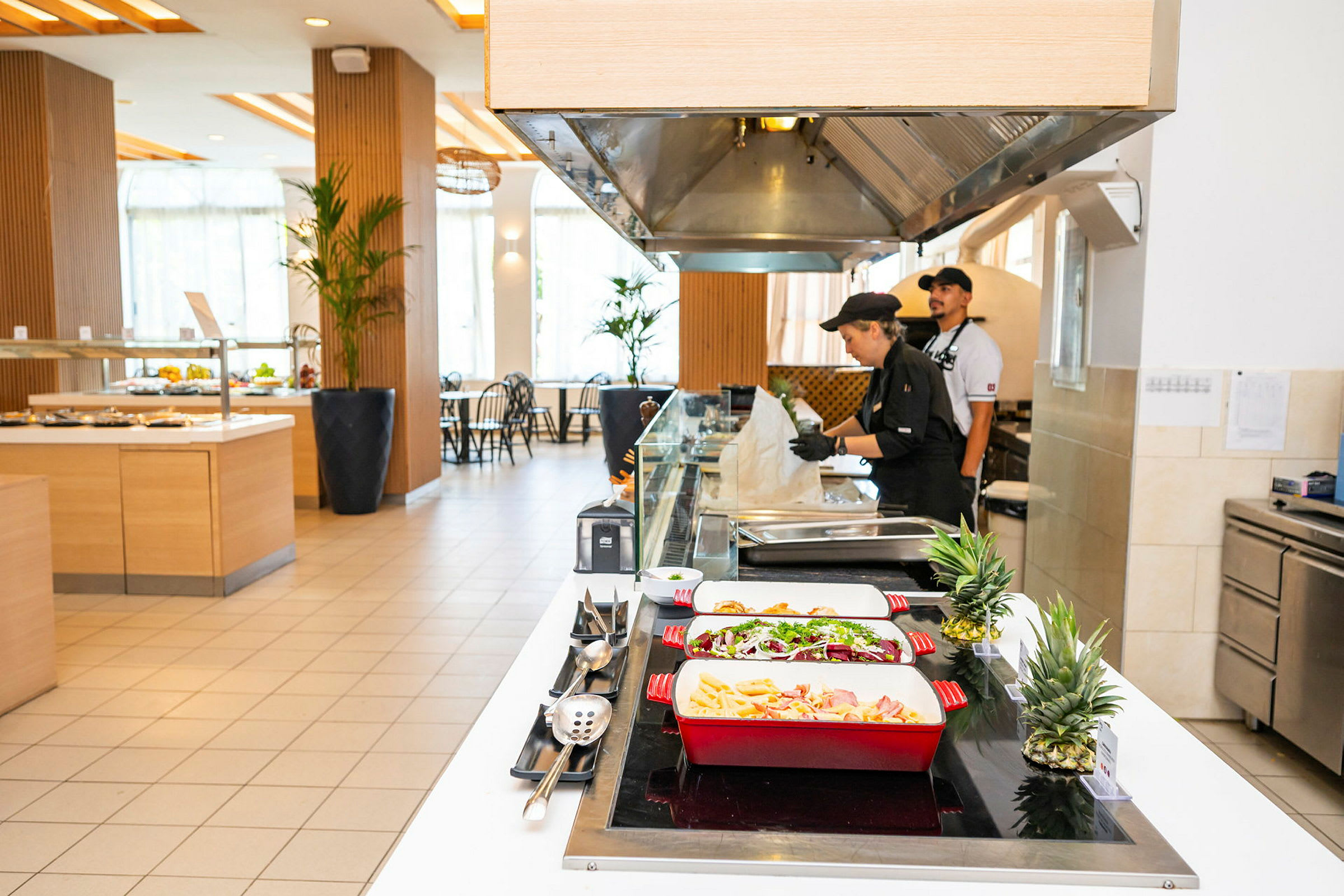 Bufféområde med mat servert i fargerike serveringsfat og kjøkkenpersonell ved arbeidsstasjon. (AI-generert tekst)