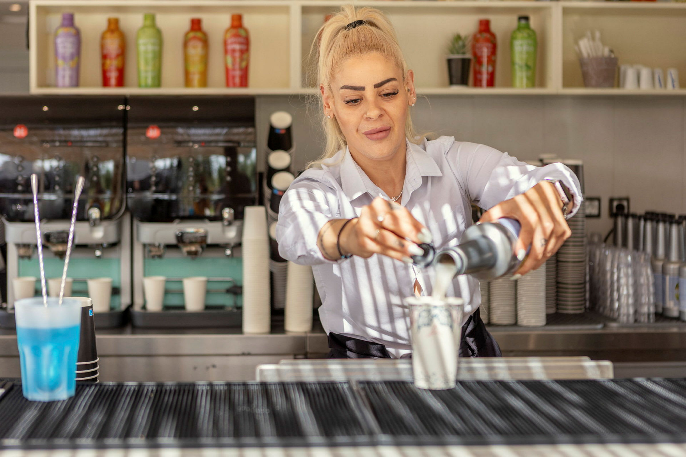 Person heller en væske i en kopp bak en kaffebar. (AI-generert tekst)