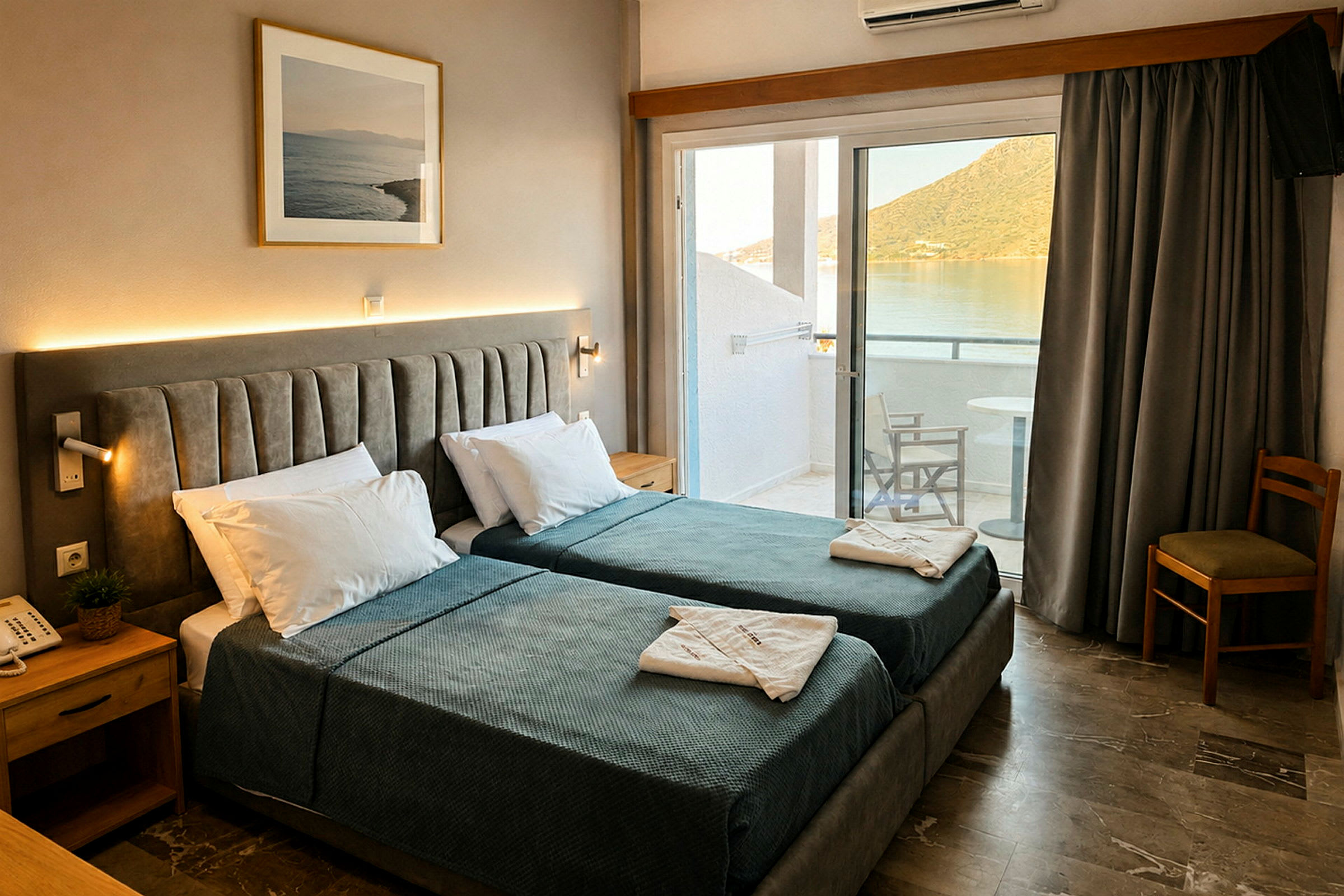 Hotellrom med to enkeltsenger, nattbord og bilde på veggen. Balkong med utsikt over vann og fjell. (AI-generert tekst)