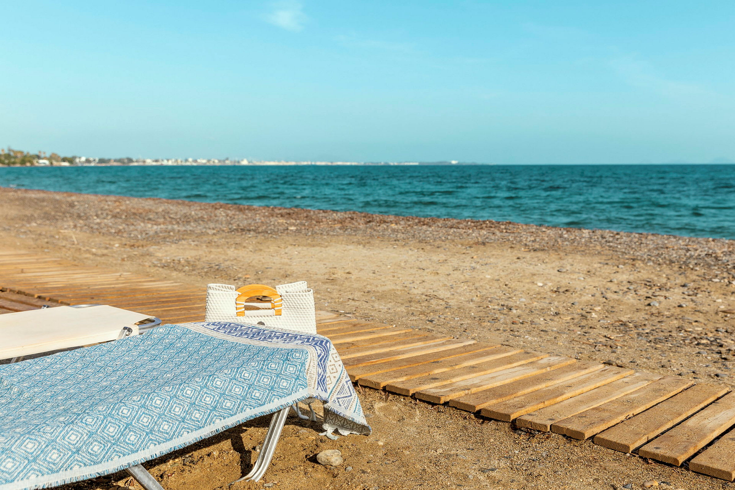 Solstol med blått håndkle og hvit veske på en strand ved havet. (AI-generert tekst)