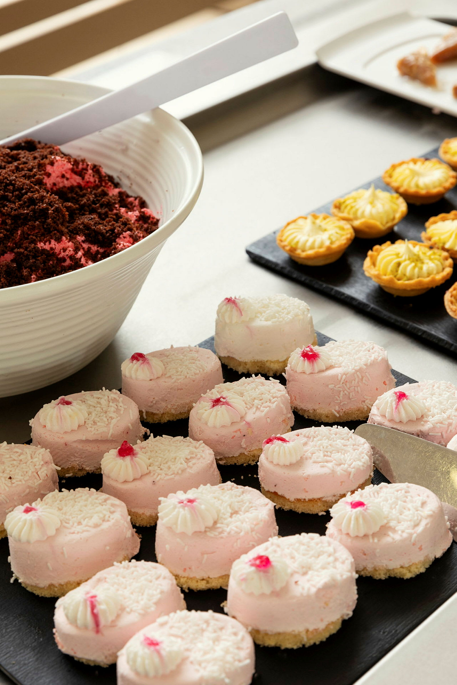 Rosa desserter med kokos og hvit topping, samt små paier i bakgrunnen. (AI-generert tekst)