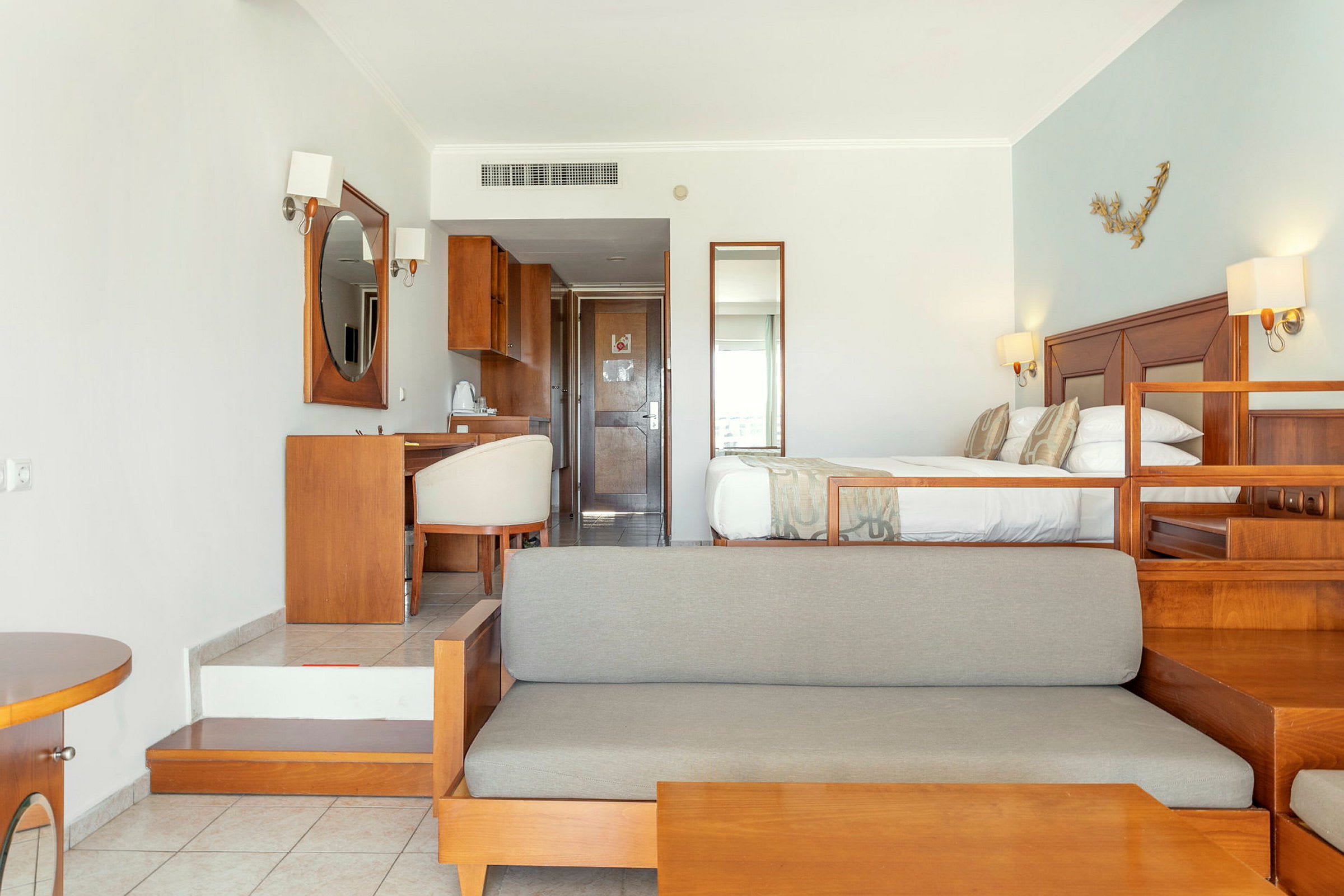 Hotellrom med seng, sofa og skrivebord i treinnredning. (AI-generert tekst)