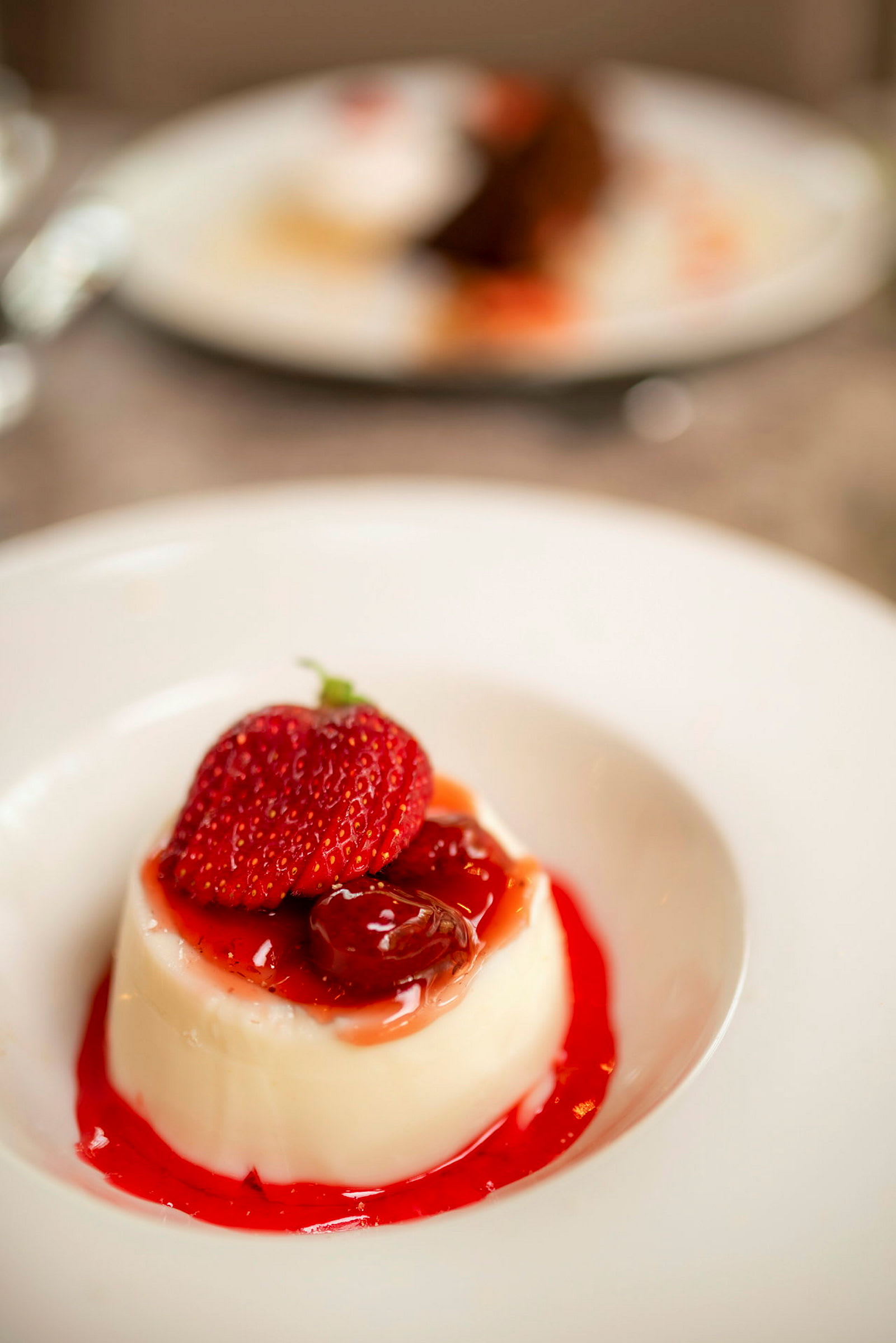 En dessert med vaniljepudding toppet med jordbær og frukt i en rød saus på en hvit tallerken. (AI-generert tekst)