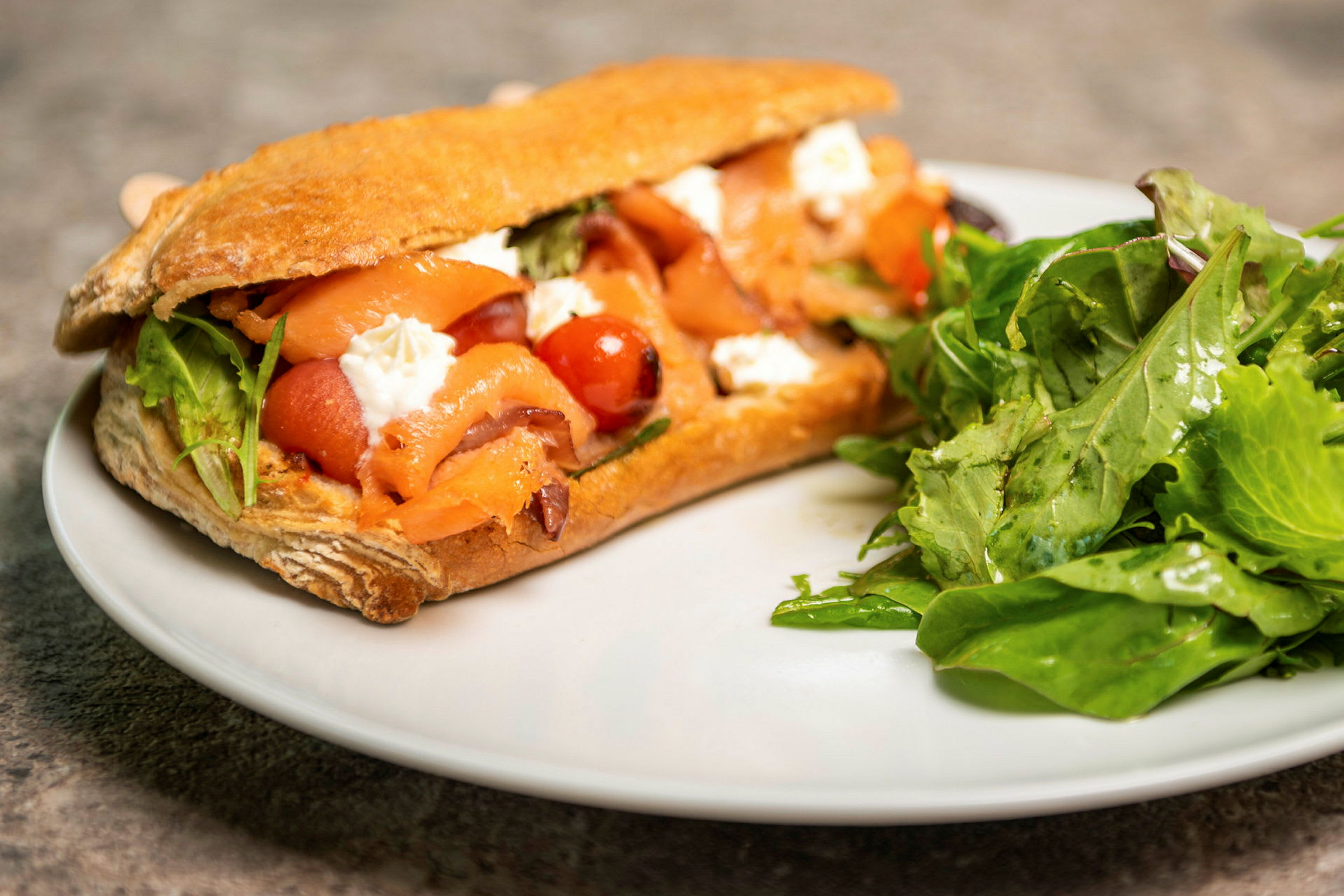 En sandwich fylt med laks, grønnsaker og ost, med en porsjon salat ved siden av. (AI-generert tekst)