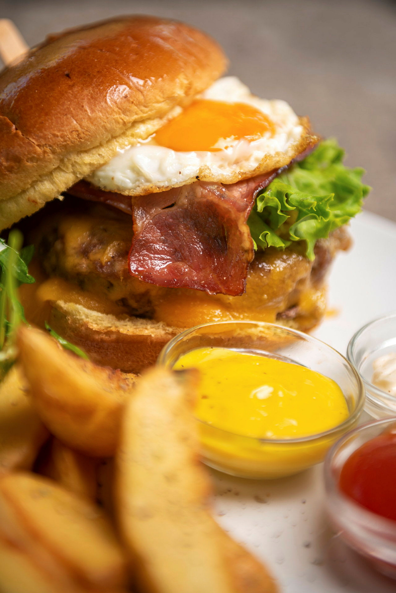En hamburger med bacon, ost, salat og stekt egg serveres med potetbåter og ulike sauser. (AI-generert tekst)