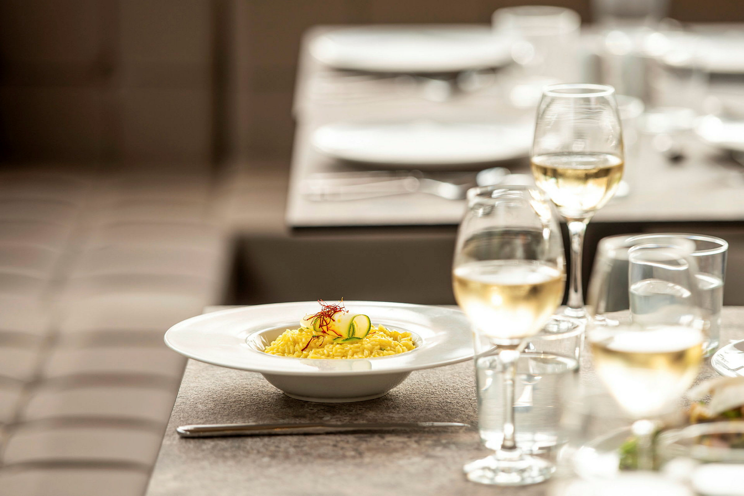 En tallerken risotto og et glass hvitvin på et dekket bord. (AI-generert tekst)