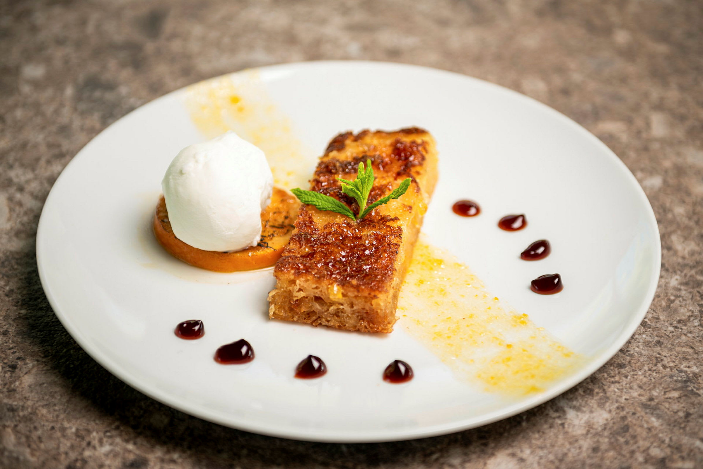 En tallerken med en dessert bestående av karamellisert brød, krem og pynt. (AI-generert tekst)